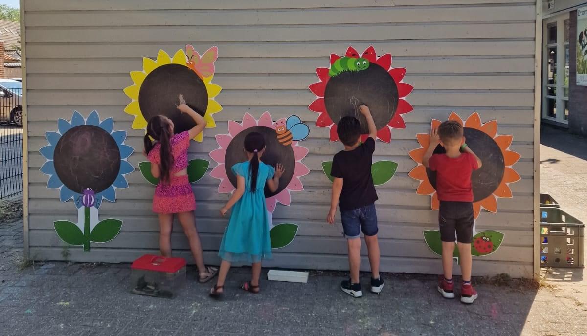 Kinderen tekenen met krijt op kleurrijke bloemenschilderingen op de muur van de school De Meander in Nieuwegein.