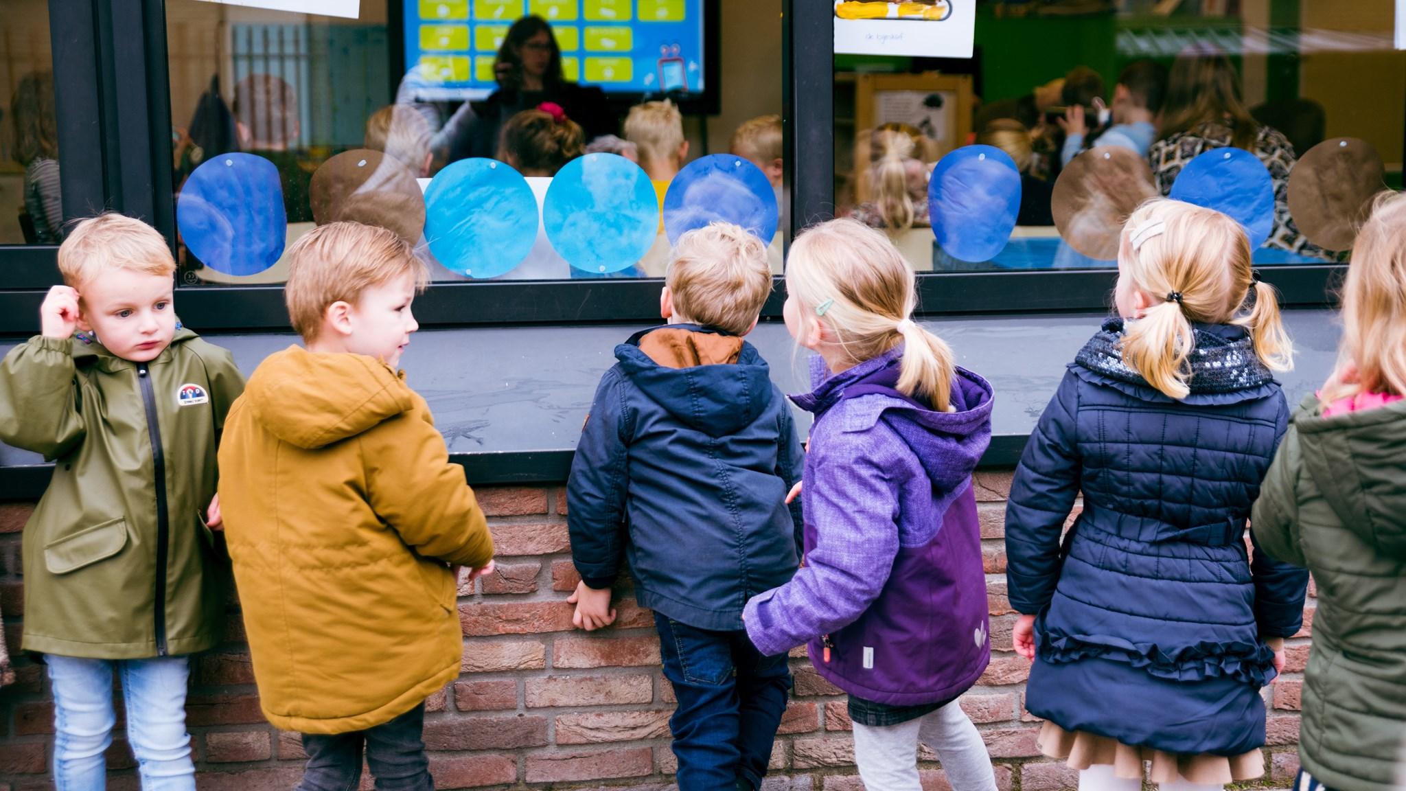 Kinderen van Basisschool met de Bijbel Het Kompas in Montfoort bekijken iets enthousiast vanachter een raam. Kinderen van Basisschool met de Bijbel Het Kompas in Montfoort bekijken iets enthousiast vanachter een raam.