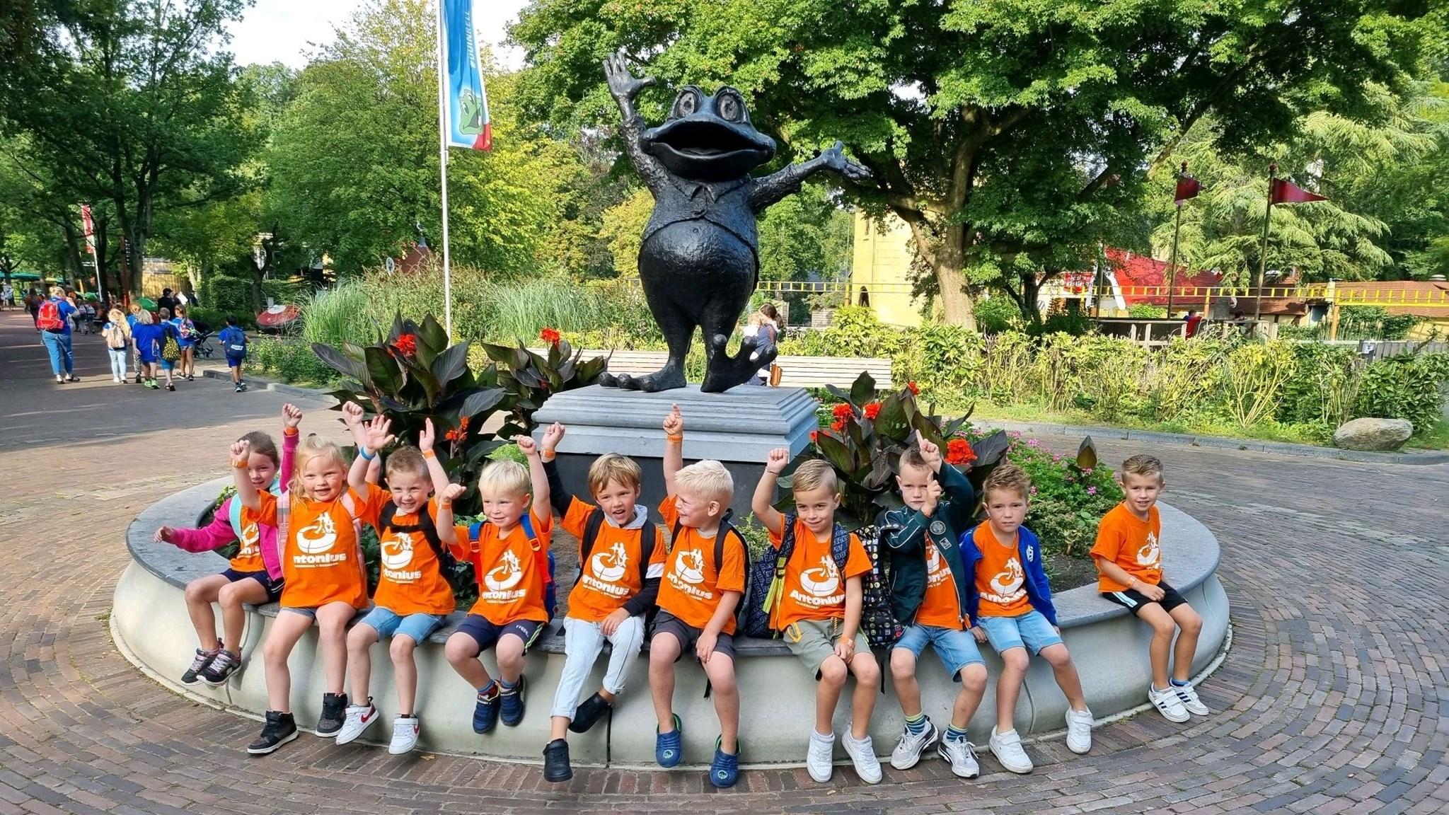 Kinderen van de Antoniusschool in Noorden zitten vrolijk bij een standbeeld in een park. Kinderen van de Antoniusschool in Noorden zitten vrolijk bij een standbeeld in een park.