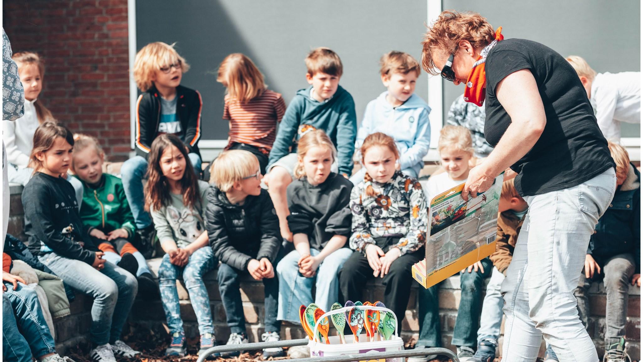 Kinderen van de Dr. De Visserschool in Breda luisteren aandachtig naar een activiteit op het schoolplein.