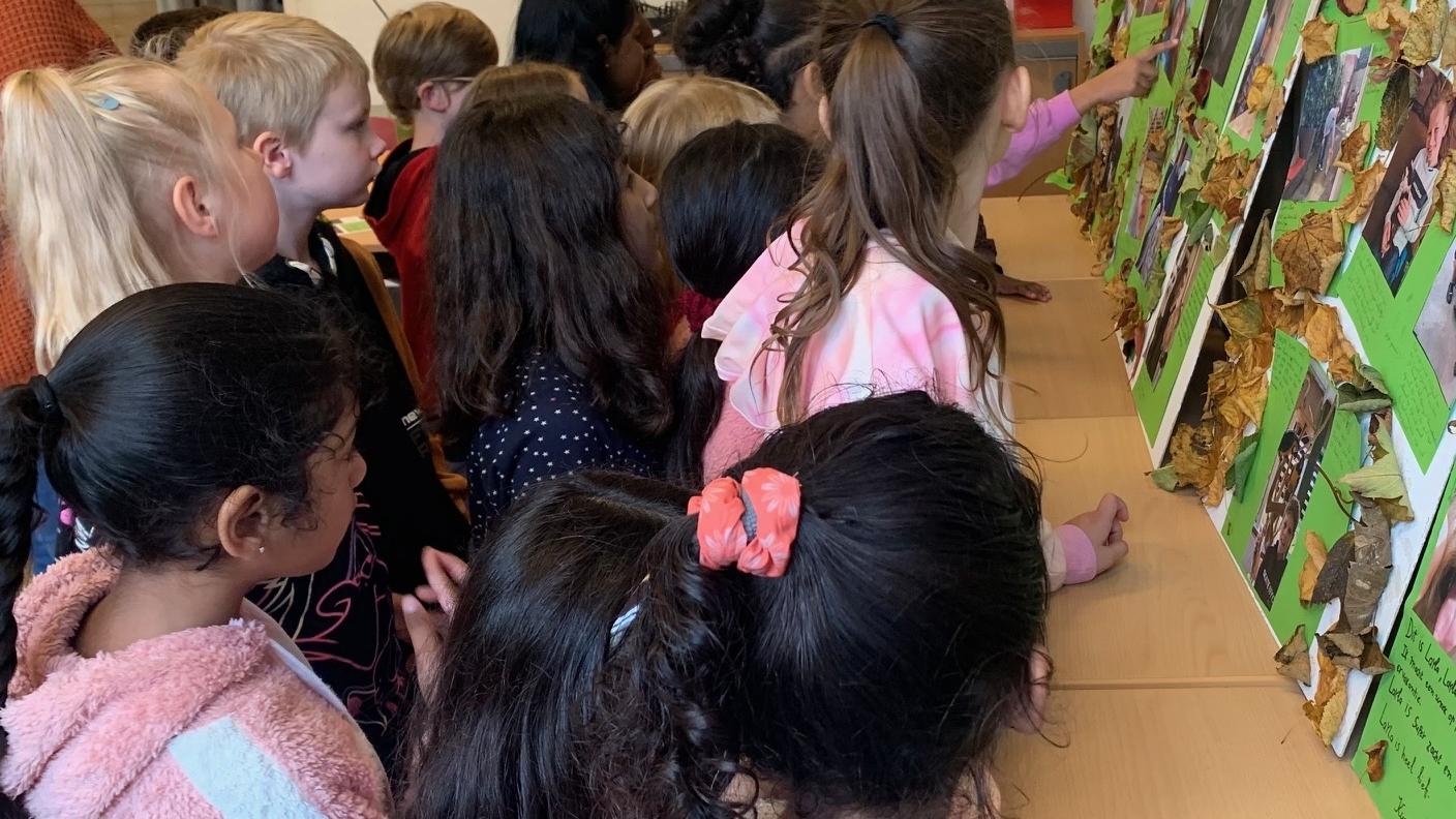 Kinderen van De Drie Linden in Den Haag kijken aandachtig naar foto's en kunst op een presentatiewand. Kinderen van De Drie Linden in Den Haag kijken aandachtig naar foto's en kunst op een presentatiewand.