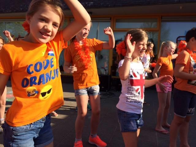 Kinderen van Dorpsschool Halle dansen vrolijk in oranje kleding tijdens een schoolfeest op het schoolplein. Kinderen van Dorpsschool Halle dansen vrolijk in oranje kleding tijdens een schoolfeest op het schoolplein.