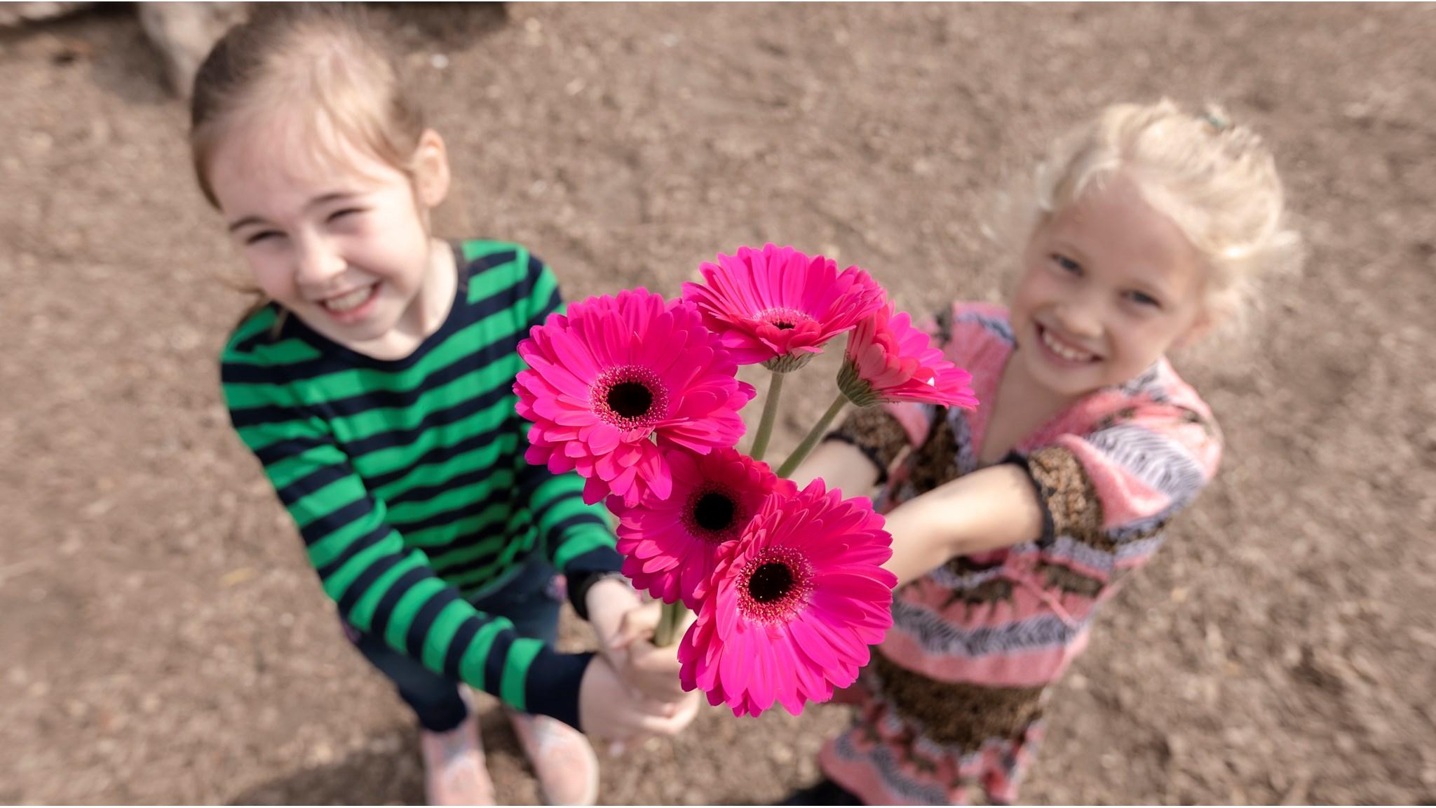 Kinderen van het Max Havelaar Kindcentrum in Delft die vrolijk een boeket met felle roze bloemen vasthouden op het schoolplein. Kinderen van het Max Havelaar Kindcentrum in Delft die vrolijk een boeket met felle roze bloemen vasthouden op het schoolplein.