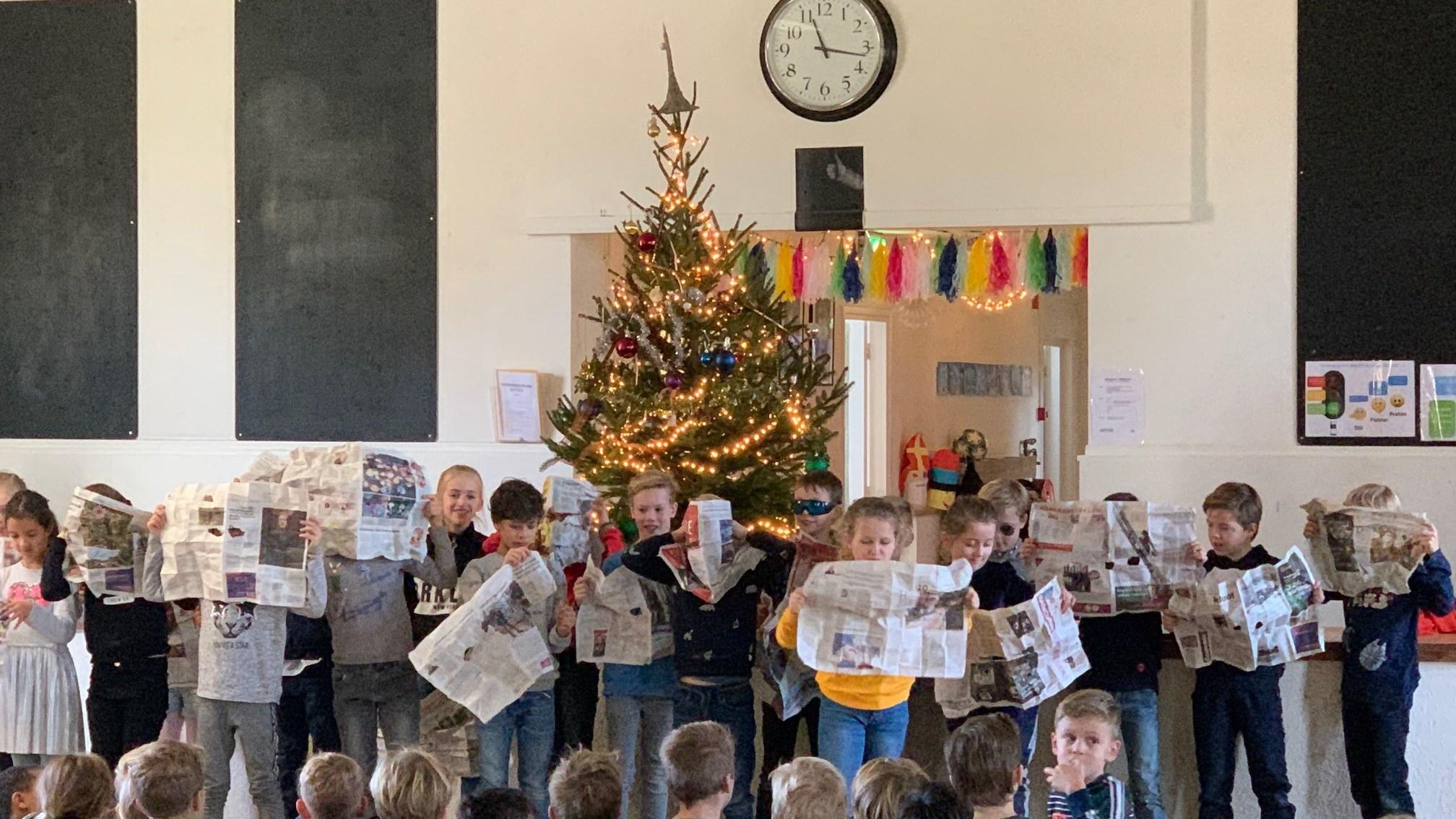 Kinderen van OBS De Muze in Nijmegen presenteren een voorstelling met kranten onder een versierde kerstboom. Kinderen van OBS De Muze in Nijmegen presenteren een voorstelling met kranten onder een versierde kerstboom.