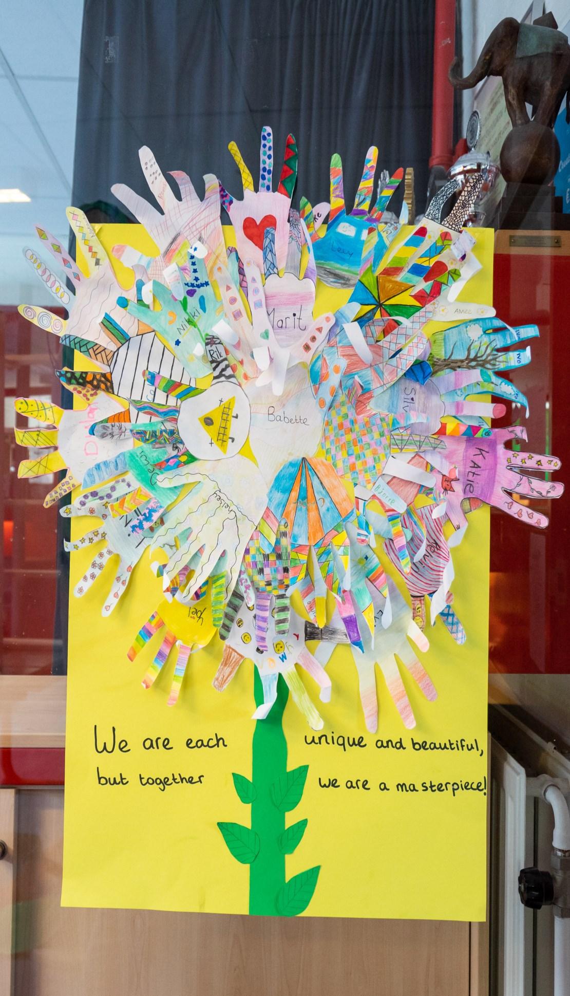 Kleurrijke handafdrukken in de vorm van een bloem met de tekst "We zijn allemaal uniek en mooi, maar samen zijn we een meesterwerk!" op Openbare Basisschool de Cocon in Alkmaar. Kleurrijke handafdrukken in de vorm van een bloem met de tekst "We zijn allemaal uniek en mooi, maar samen zijn we een meesterwerk!" op Openbare Basisschool de Cocon in Alkmaar.