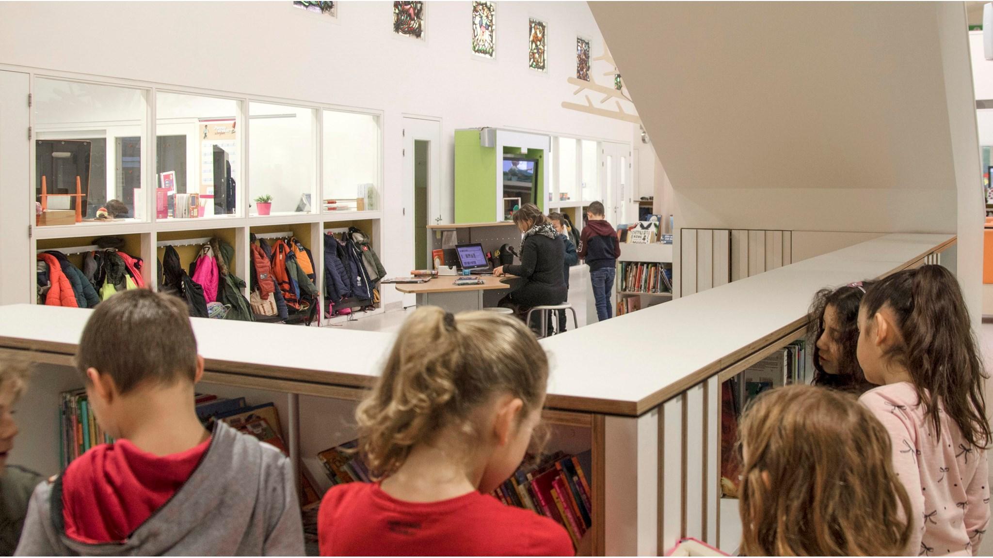 KOC De Brakken in Rijen, leerlingen kijken naar boeken terwijl een leerkracht aan een computer werkt. KOC De Brakken in Rijen, leerlingen kijken naar boeken terwijl een leerkracht aan een computer werkt.