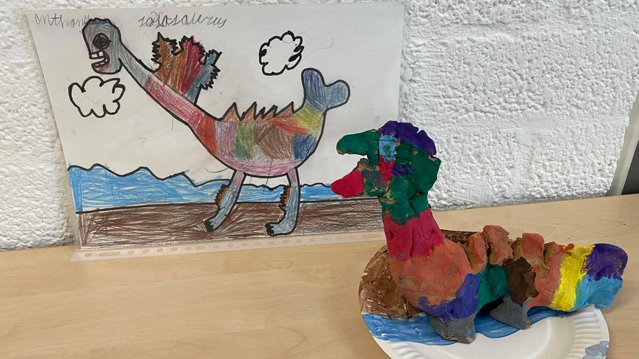 Kunstwerken van leerlingen van Openbare Basisschool Dakpark in Rotterdam, inclusief een kleurige dinosaurustekening en een kleimodel. Kunstwerken van leerlingen van Openbare Basisschool Dakpark in Rotterdam, inclusief een kleurige dinosaurustekening en een kleimodel.
