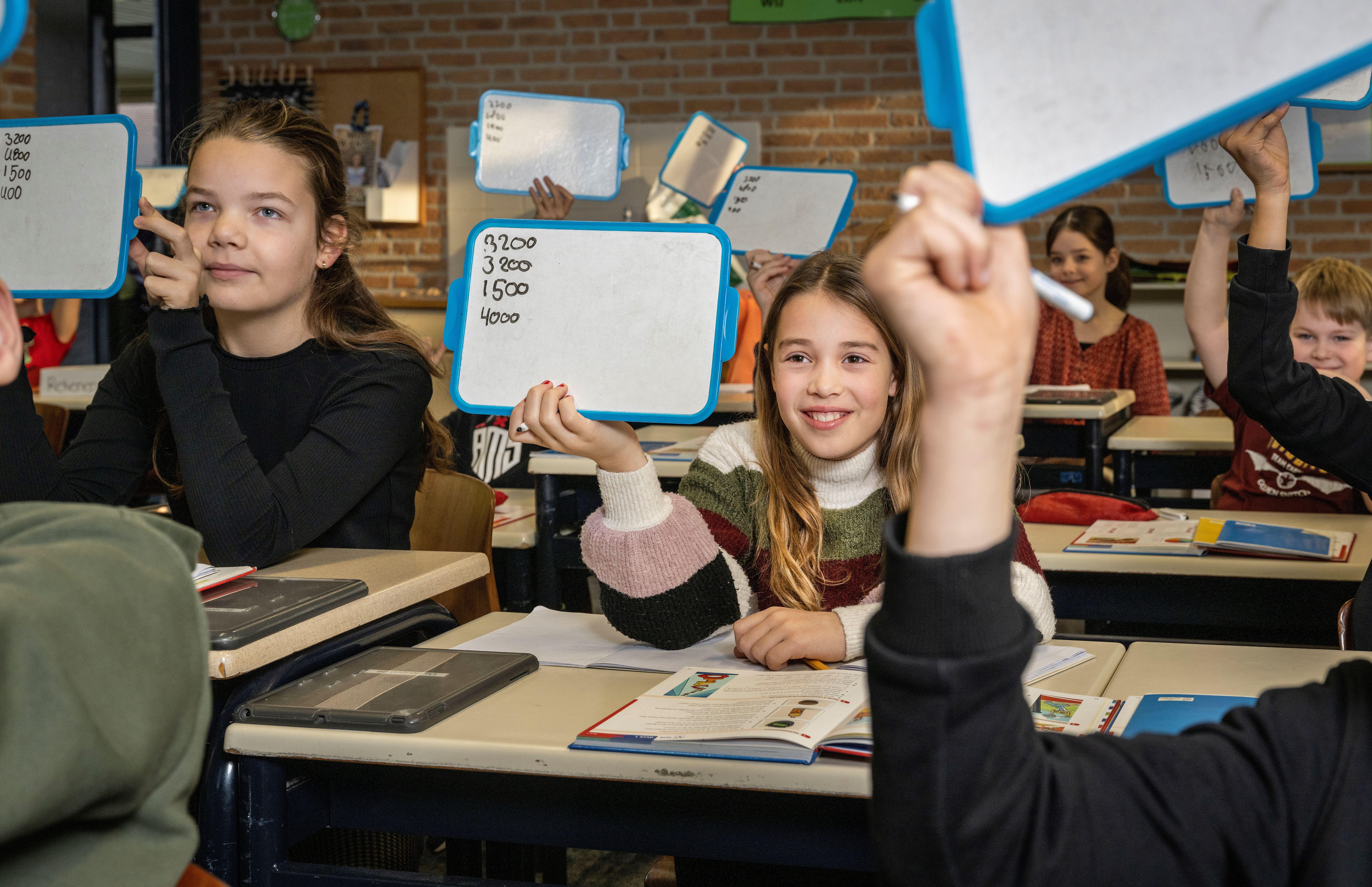 Leerlingen in Basisschool De Horizon in Grashoek zijn actief betrokken bij de les en houden antwoorden omhoog op whiteboards. Leerlingen in Basisschool De Horizon in Grashoek zijn actief betrokken bij de les en houden antwoorden omhoog op whiteboards.