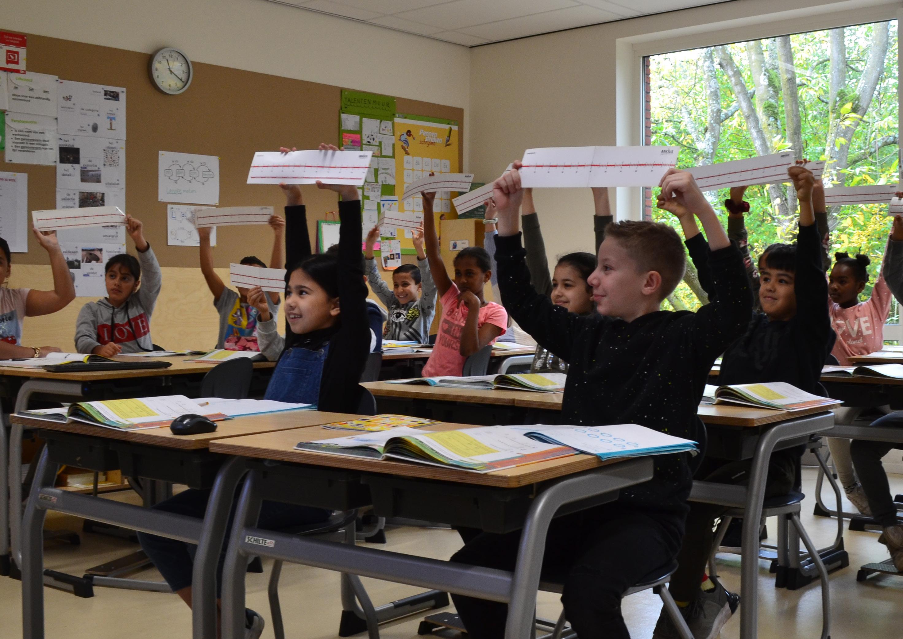 Leerlingen in de Burgemeester De Vlugtschool in Amsterdam steken enthousiast hun werkbladen omhoog tijdens een les. Leerlingen in de Burgemeester De Vlugtschool in Amsterdam steken enthousiast hun werkbladen omhoog tijdens een les.
