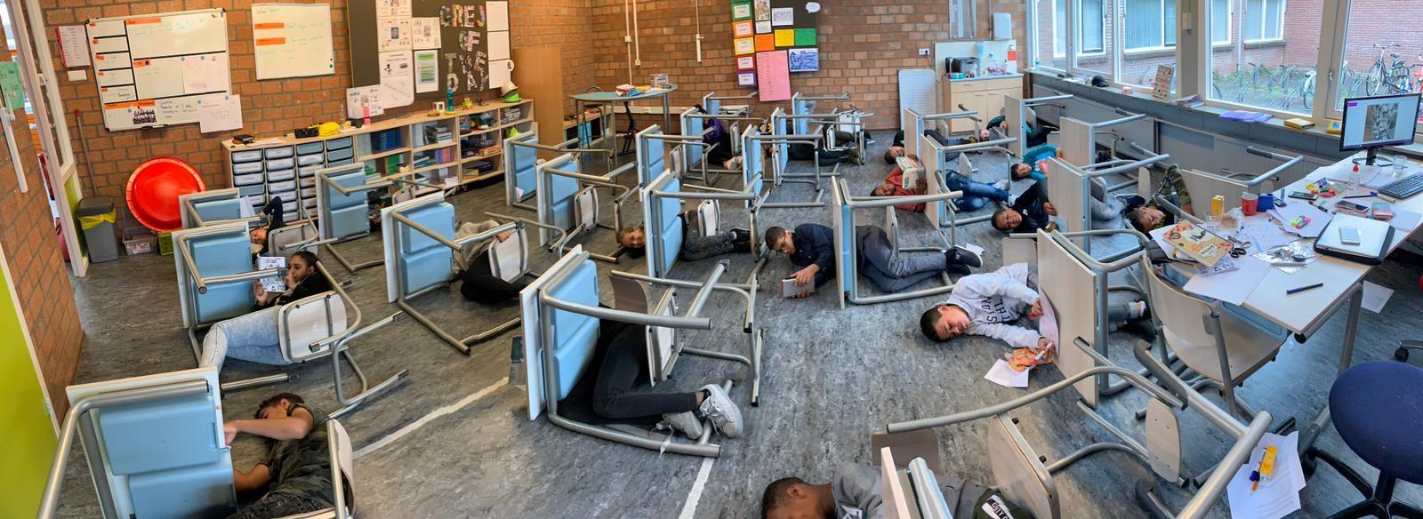 Leerlingen liggen op de grond tussen ondersteboven gekeerde stoelen in het klaslokaal van De Akkers in Spijkenisse. Leerlingen liggen op de grond tussen ondersteboven gekeerde stoelen in het klaslokaal van De Akkers in Spijkenisse.