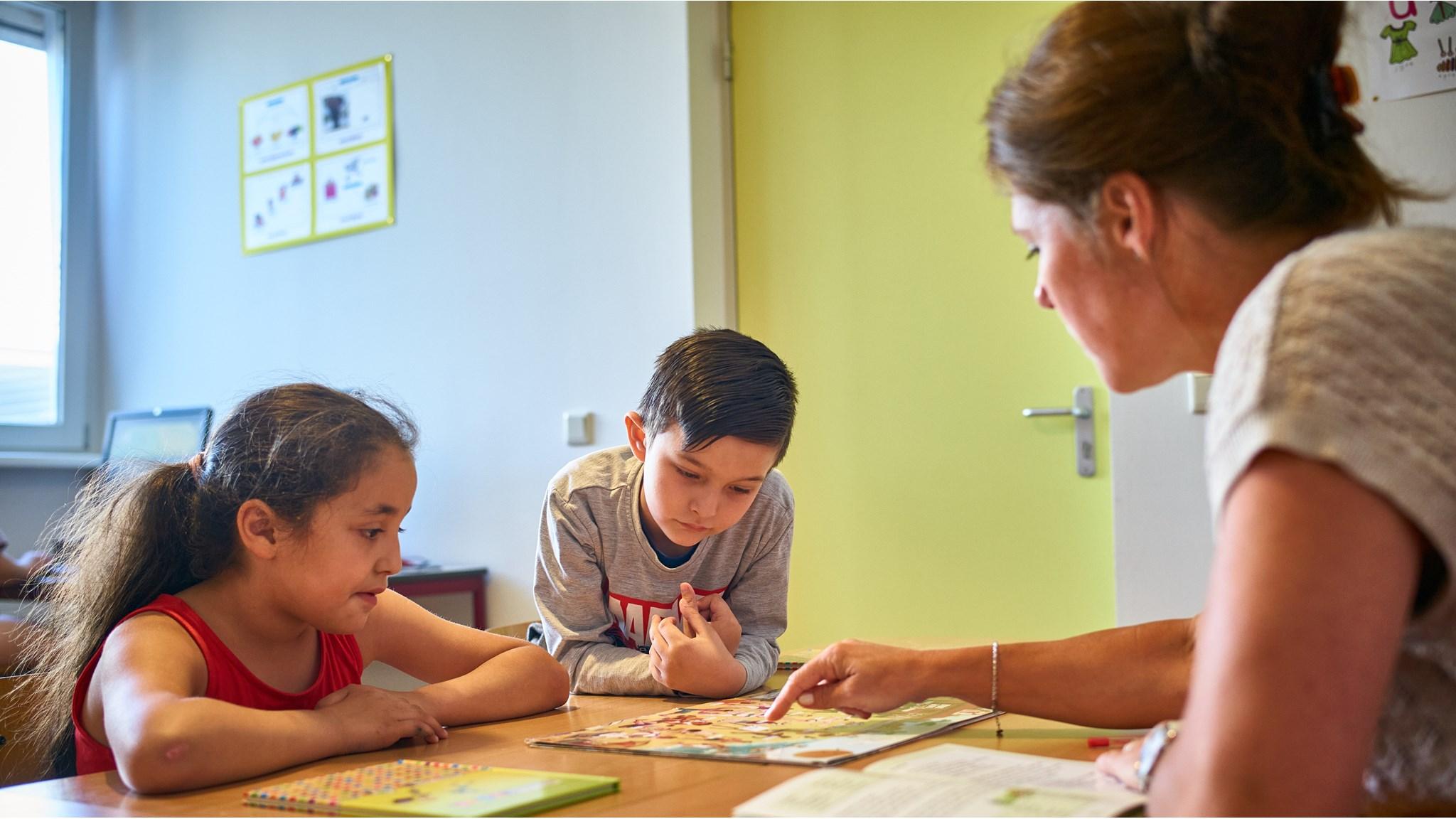 Leerlingen van Basisschool De Krabbenkooi in Bergen op Zoom bekijken samen een boek met hun docente. Leerlingen van Basisschool De Krabbenkooi in Bergen op Zoom bekijken samen een boek met hun docente.