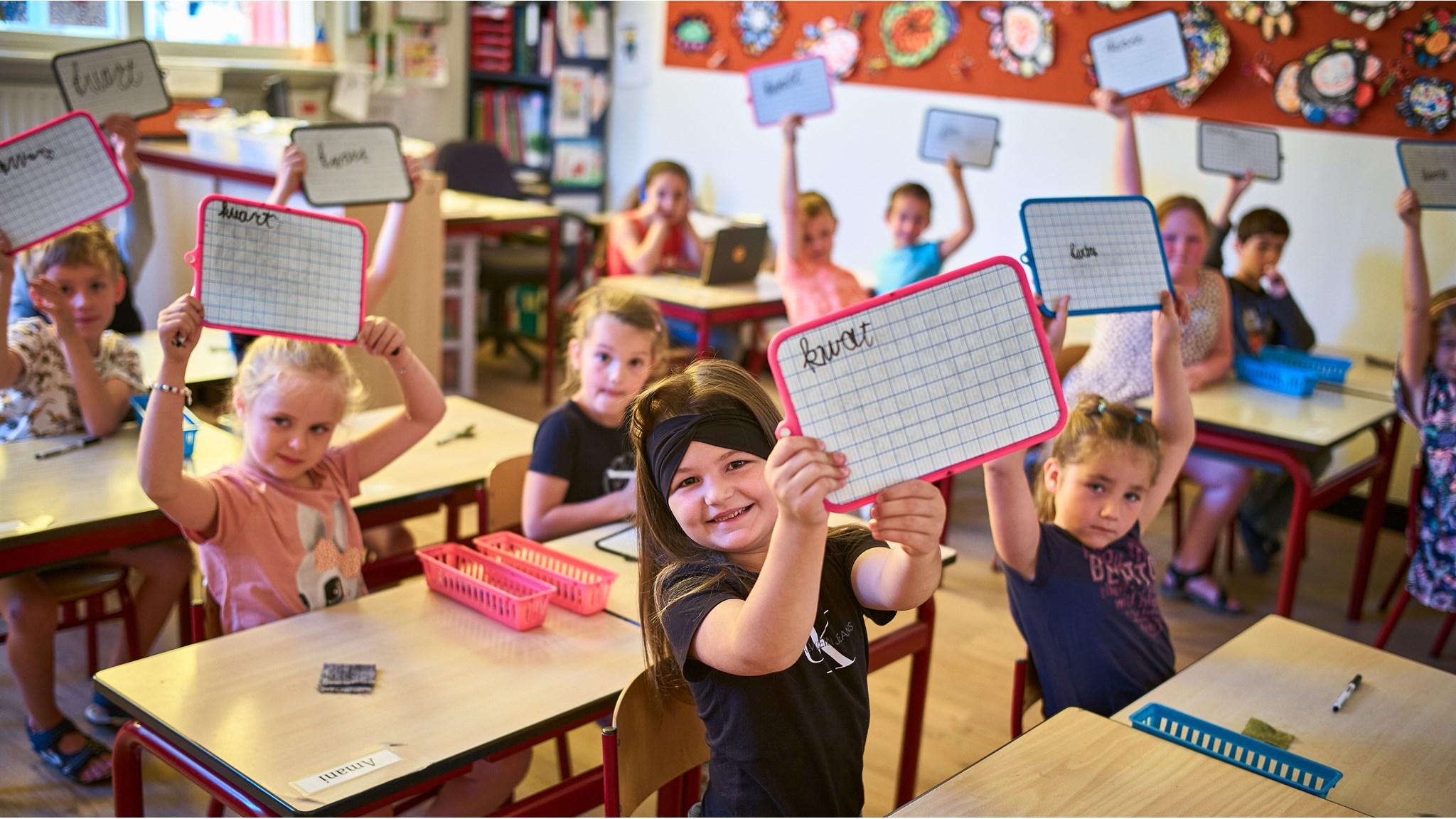 Leerlingen van Basisschool De Krabbenkooi in Bergen op Zoom houden met enthousiasme hun schrijfbordjes omhoog tijdens een les. Leerlingen van Basisschool De Krabbenkooi in Bergen op Zoom houden met enthousiasme hun schrijfbordjes omhoog tijdens een les.