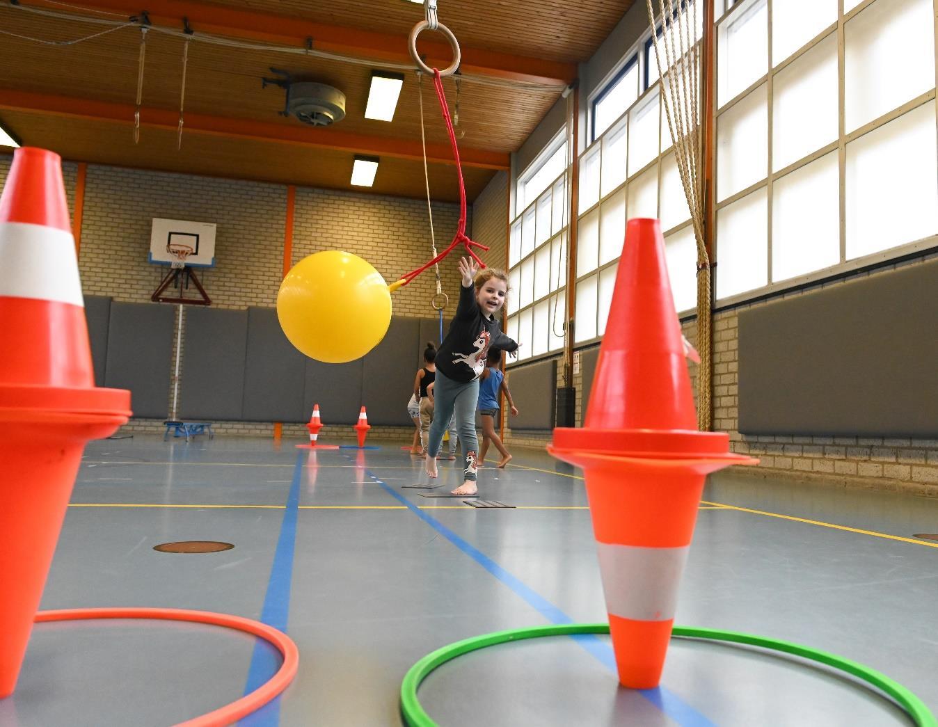 Leerlingen van basisschool De Pionier in Rotterdam spelen actief in de gymzaal met hindernissen en een gele bal. Leerlingen van basisschool De Pionier in Rotterdam spelen actief in de gymzaal met hindernissen en een gele bal.