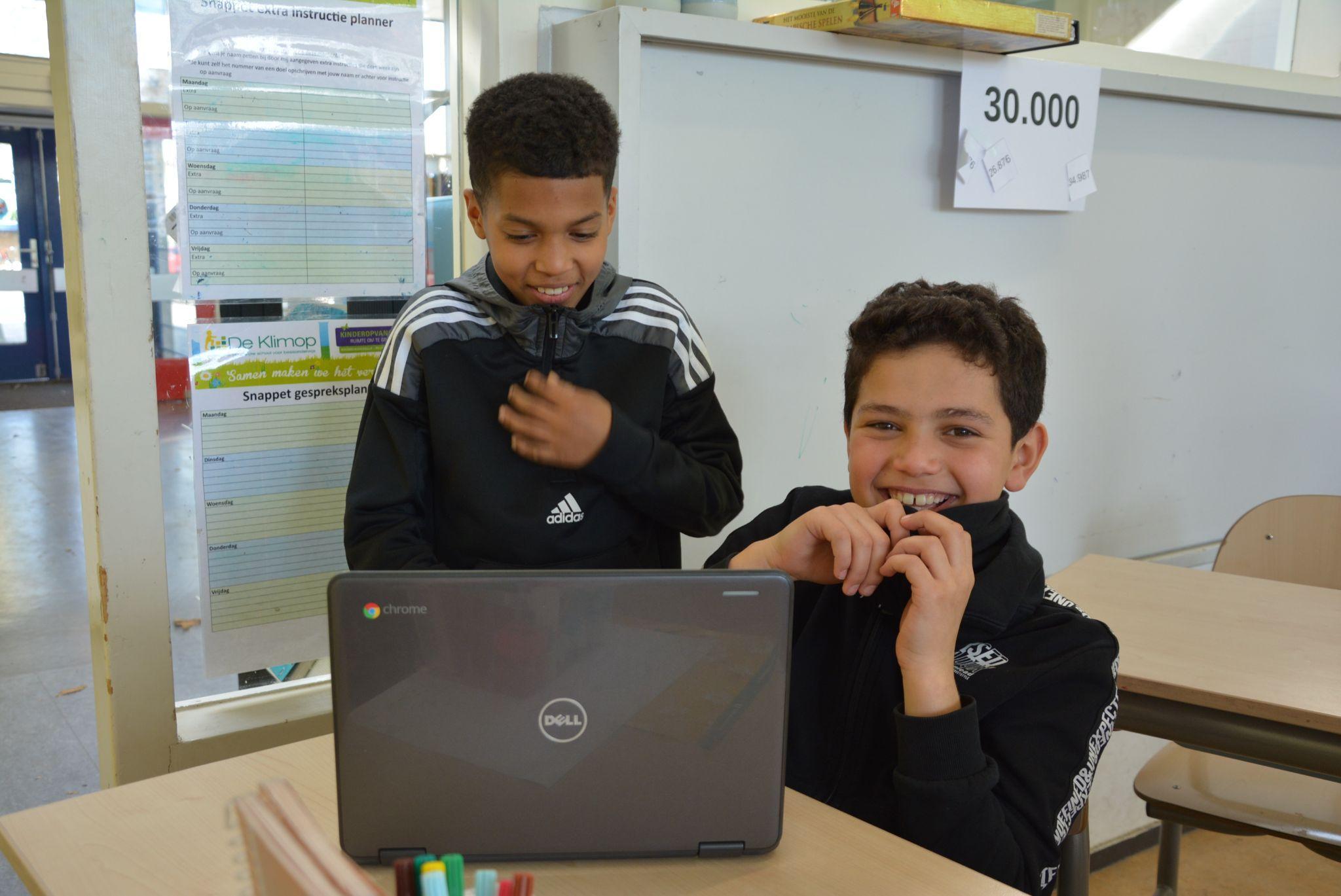 Leerlingen van CBS De Klimop in Ridderkerk werken glimlachend aan een laptop in de klas. Leerlingen van CBS De Klimop in Ridderkerk werken glimlachend aan een laptop in de klas.