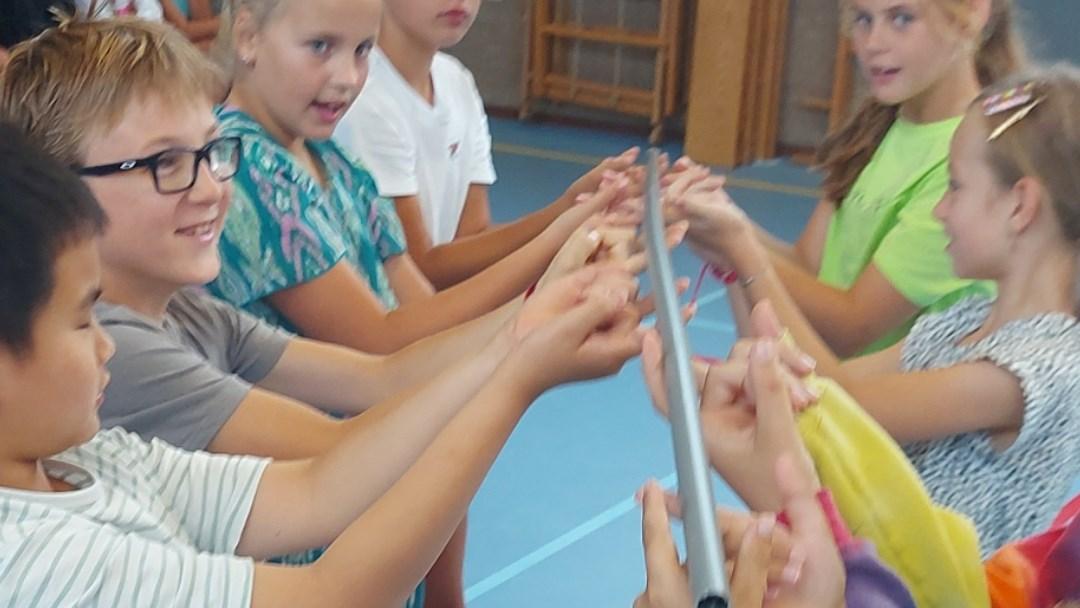 Leerlingen van de Antoniusschool in Noorden participeren in een groepsactiviteit met een lang stuk materiaal in de gymzaal. Leerlingen van de Antoniusschool in Noorden participeren in een groepsactiviteit met een lang stuk materiaal in de gymzaal.