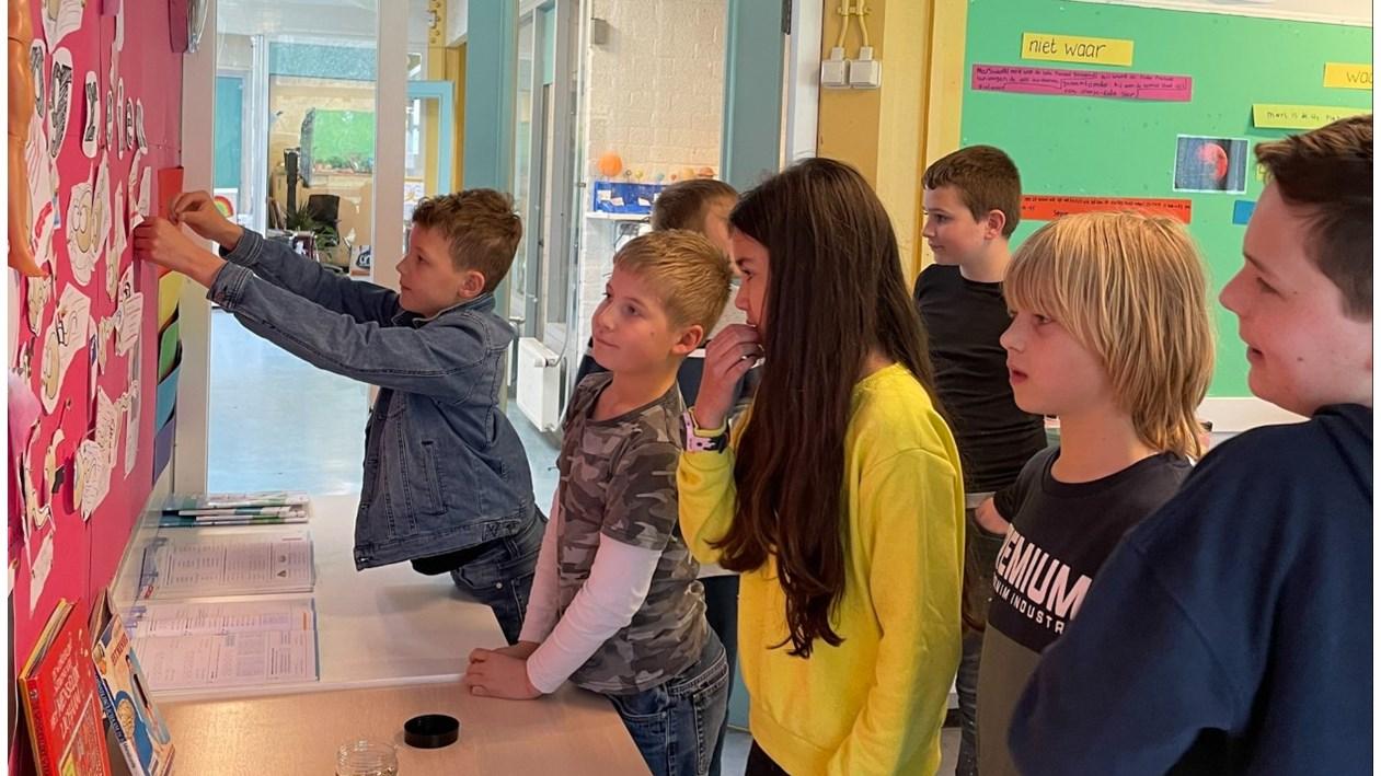 Leerlingen van De Twine in IJlst bekijken en interageren met een kleurrijke muur vol creatieve opdrachten.