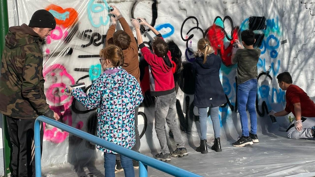Leerlingen van De Twine in IJlst zijn bezig met het schilderen van een muur op het schoolplein.