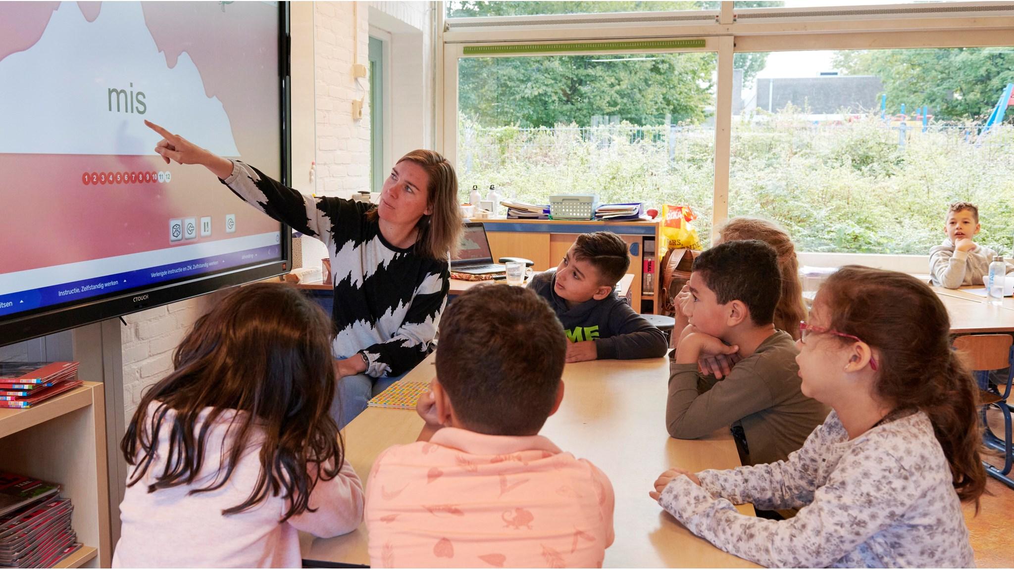 Leerlingen van OBS de Globe in Haarlem volgen een les met een docente die hen iets uitlegt op een digitaal bord. Leerlingen van OBS de Globe in Haarlem volgen een les met een docente die hen iets uitlegt op een digitaal bord.