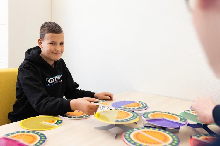 Leerlingen van 't PuzzelsTuk in Tuk spelen een spel met kleurrijke schijven aan tafel. Leerlingen van 't PuzzelsTuk in Tuk spelen een spel met kleurrijke schijven aan tafel.