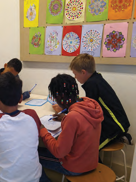 Leerlingen werken samen aan tekeningen in De Vlierboom in Den Haag, omgeven door kleurrijke kunstwerken aan de muur. Leerlingen werken samen aan tekeningen in De Vlierboom in Den Haag, omgeven door kleurrijke kunstwerken aan de muur.
