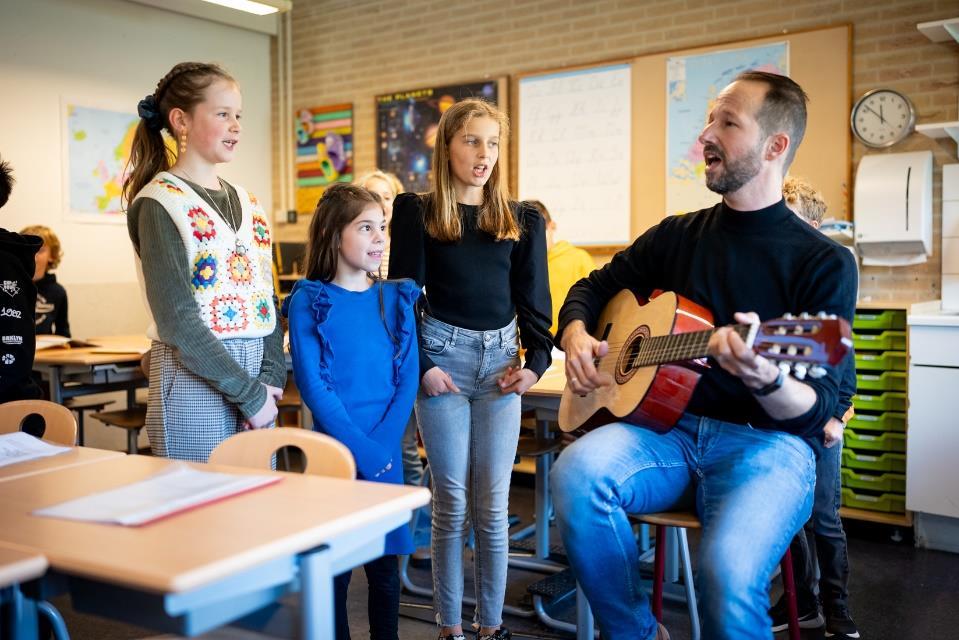 Leerlingen zingen samen met hun leraar gitaarspelend in Openbare Basisschool De Samensprong in Grubbenvorst. Leerlingen zingen samen met hun leraar gitaarspelend in Openbare Basisschool De Samensprong in Grubbenvorst.