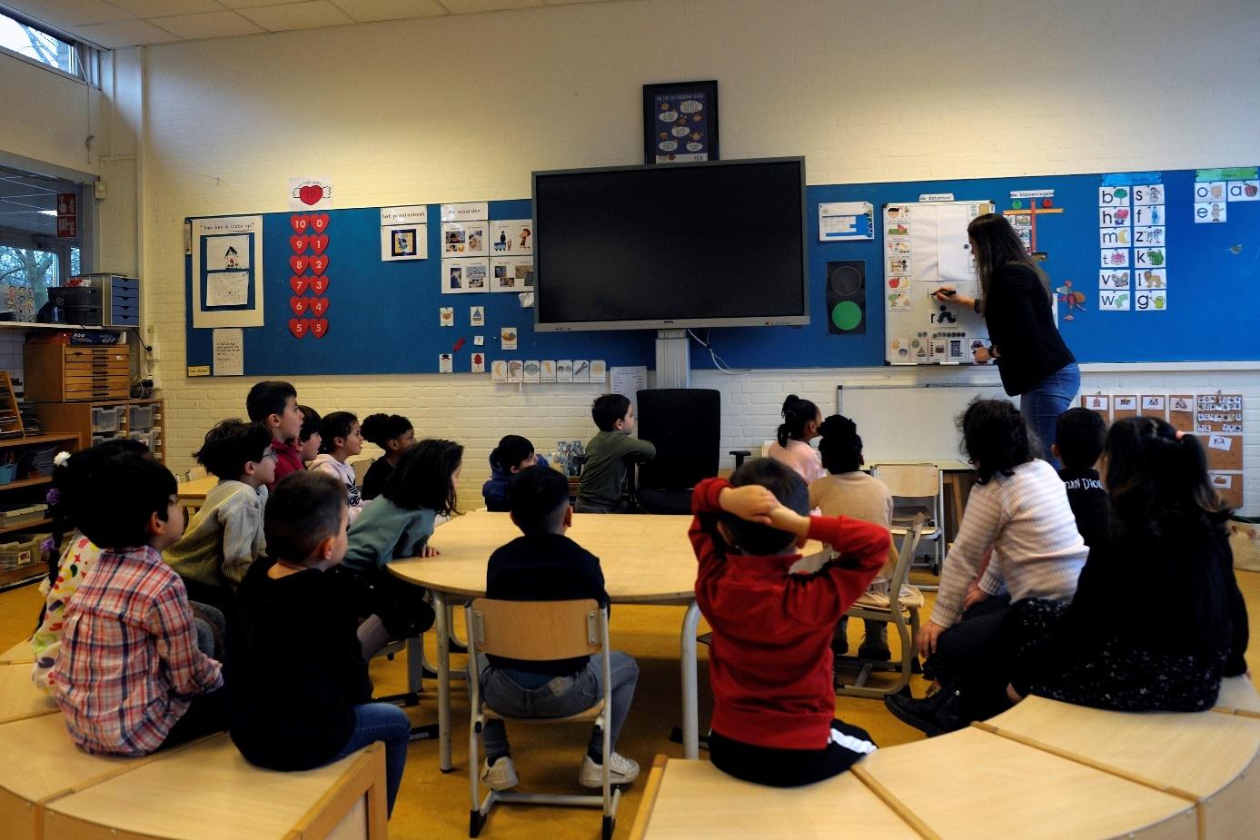 Leerlingen zitten in de klas van RK basisschool Paus Joannes in Zaandam terwijl een lerares iets op het bord uitlegt. Leerlingen zitten in de klas van RK basisschool Paus Joannes in Zaandam terwijl een lerares iets op het bord uitlegt.
