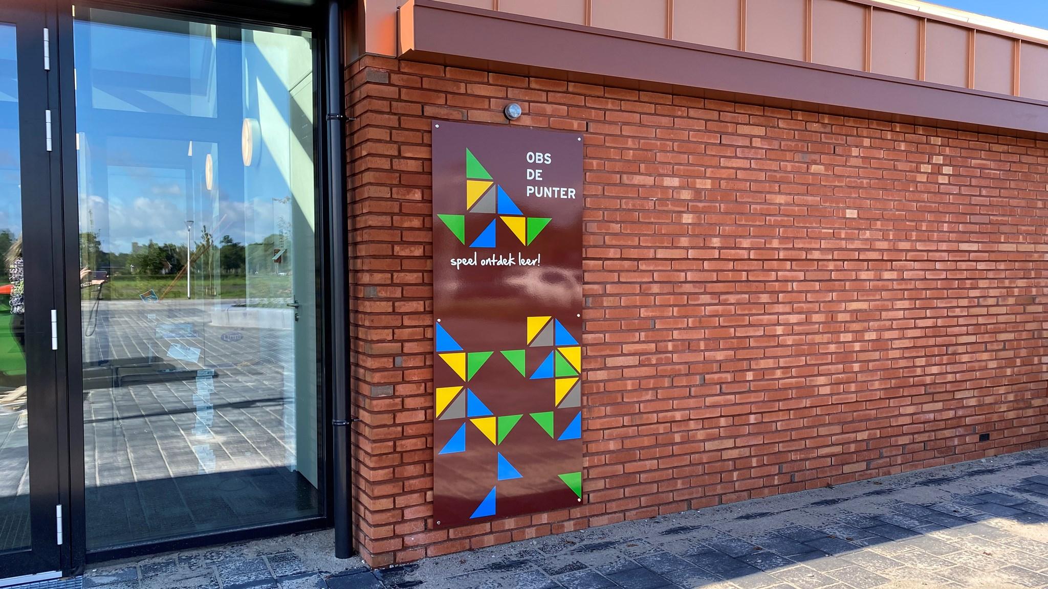 OBS De Punter in Giethoorn toont een kleurrijk schoolplein met het motto "speel ontdek leer!" op een wandbord.