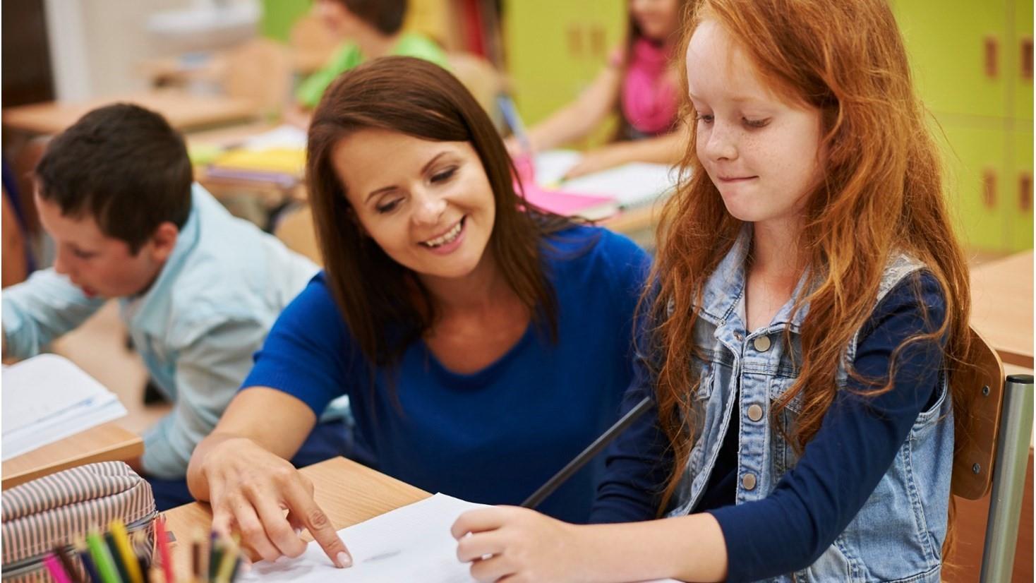 Onderwijsactiviteit bij Basisschool De Regenboog in Schaijk, waar een lerares een meisje helpt met haar schoolwerk. Onderwijsactiviteit bij Basisschool De Regenboog in Schaijk, waar een lerares een meisje helpt met haar schoolwerk.