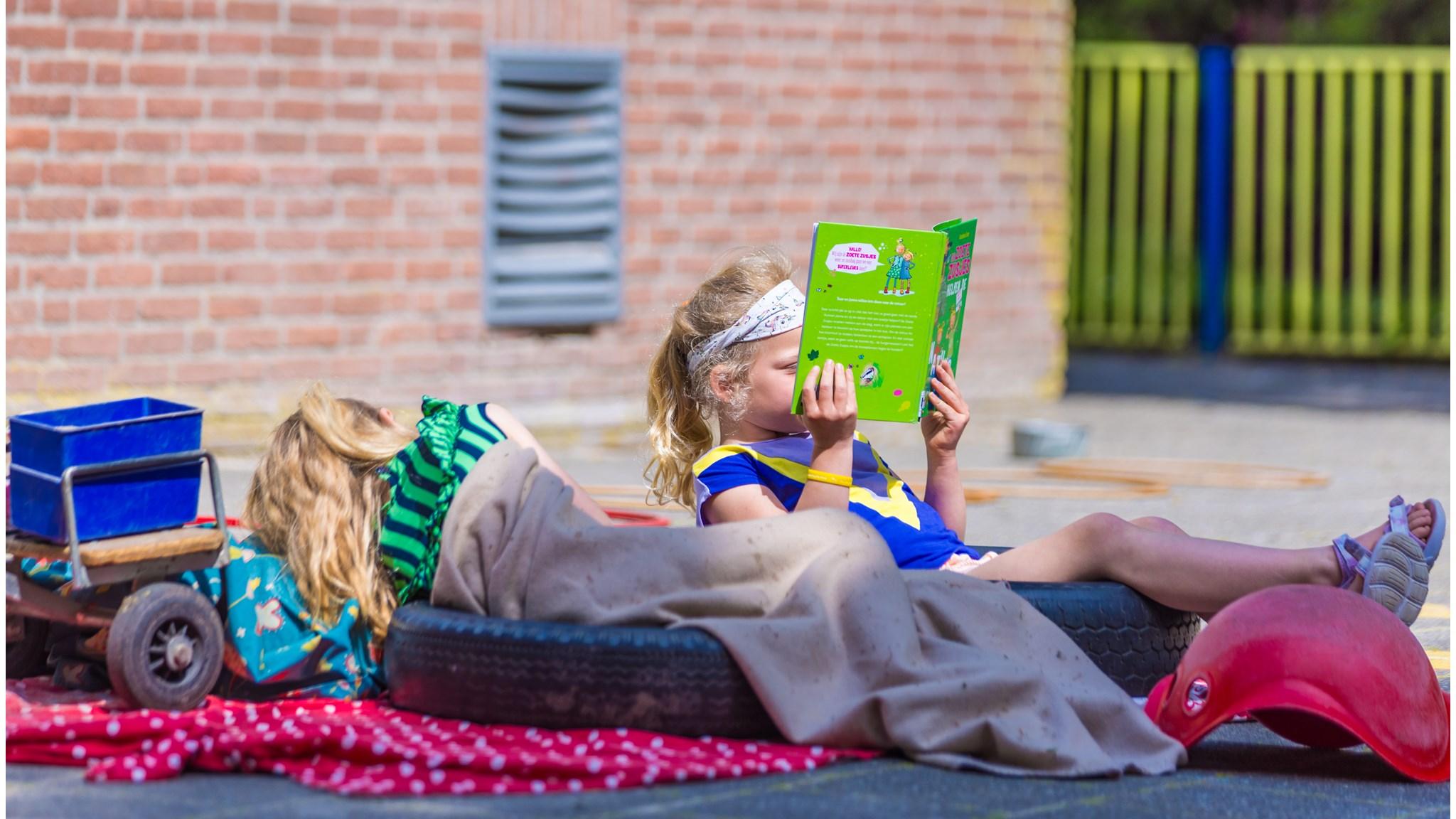 Op het schoolplein van Basisschool De Triangel in Grijpskerk ontspannen kinderen met boeken en speeltuinmateriaal.