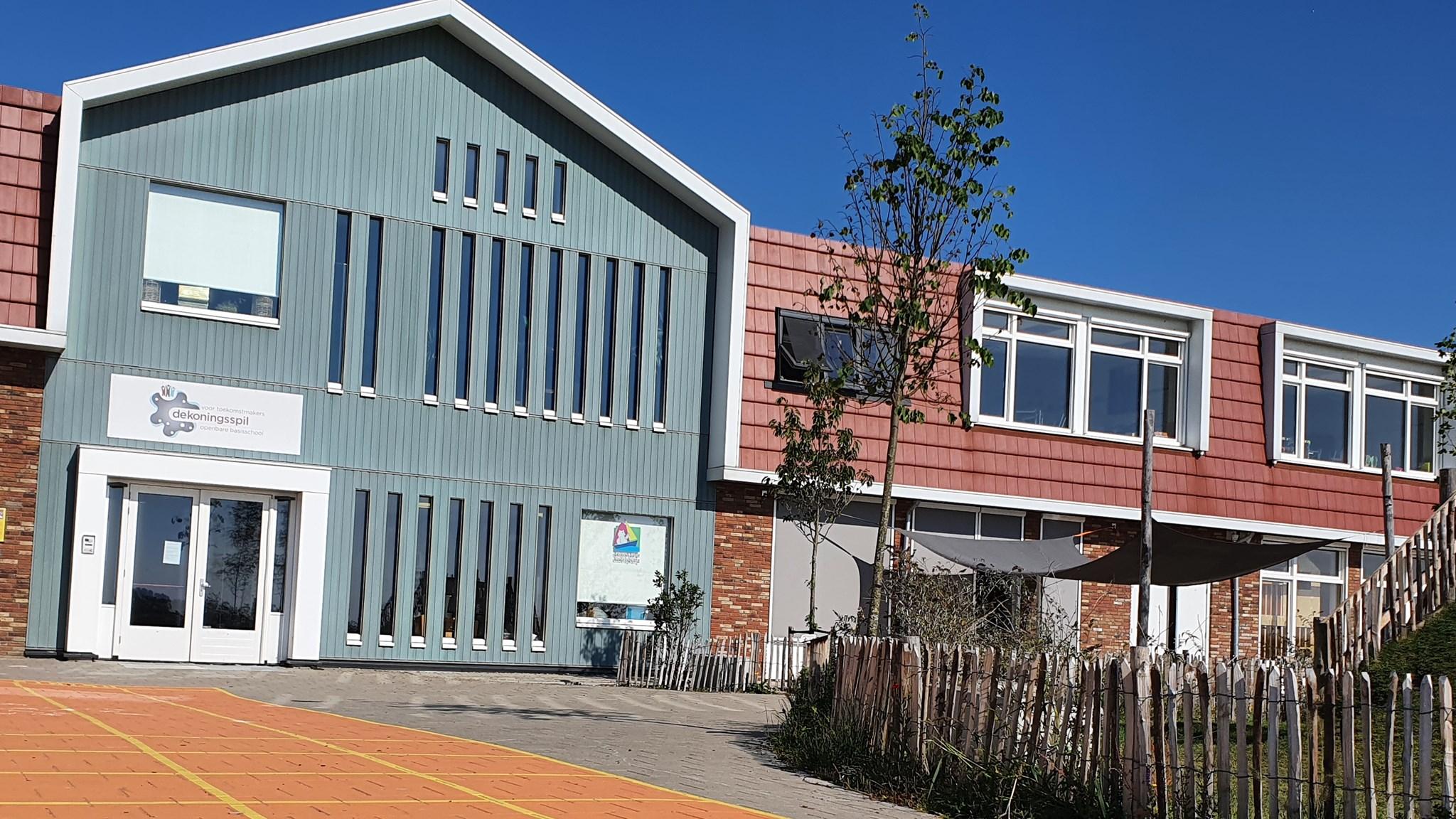 Openbare Basisschool De Koningsspil in Oosthuizen, met een helder blauwe lucht en een kleurrijk schoolplein.