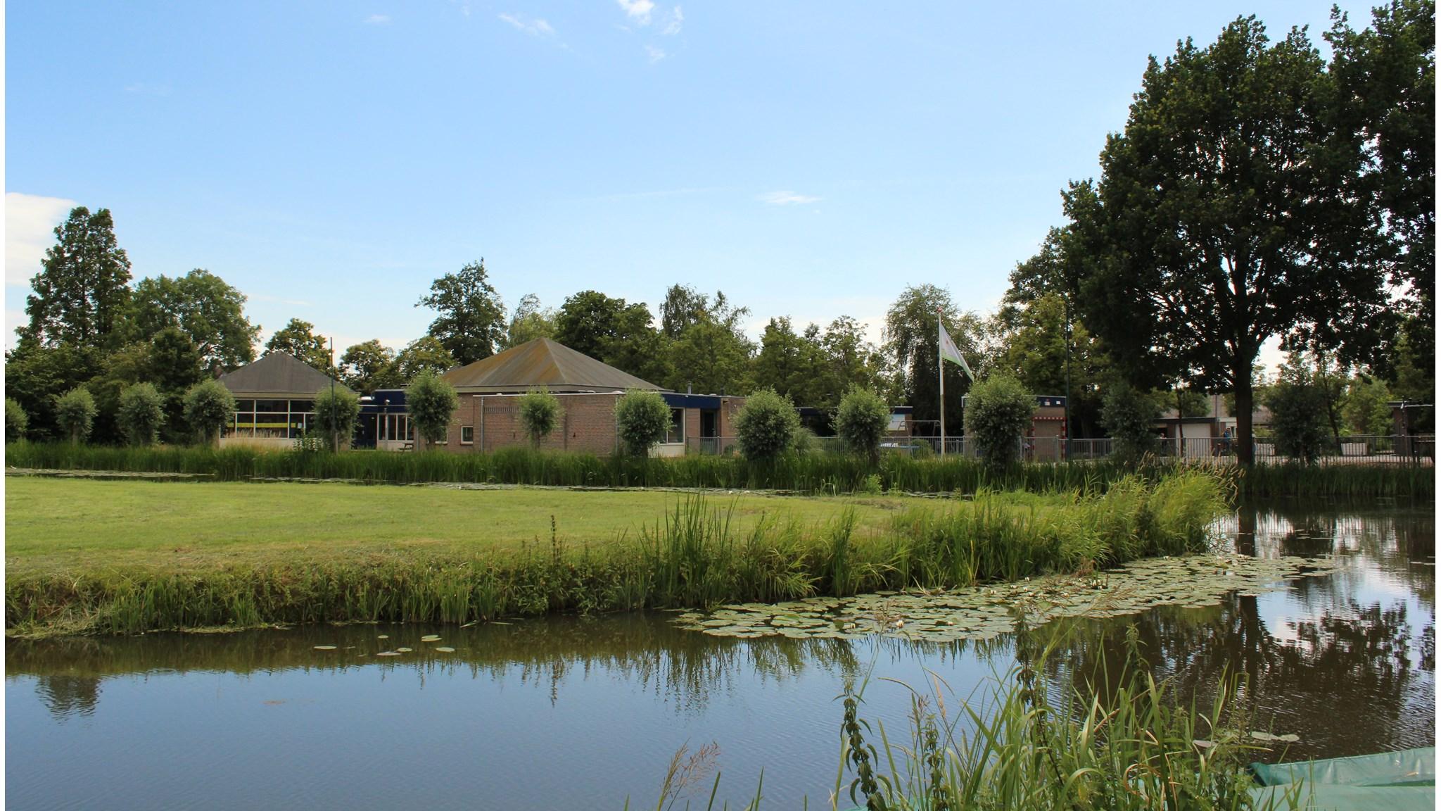 Openbare Basisschool de Vijzel in Hauwert met een groen schoolplein en omliggend water. Openbare Basisschool de Vijzel in Hauwert met een groen schoolplein en omliggend water.
