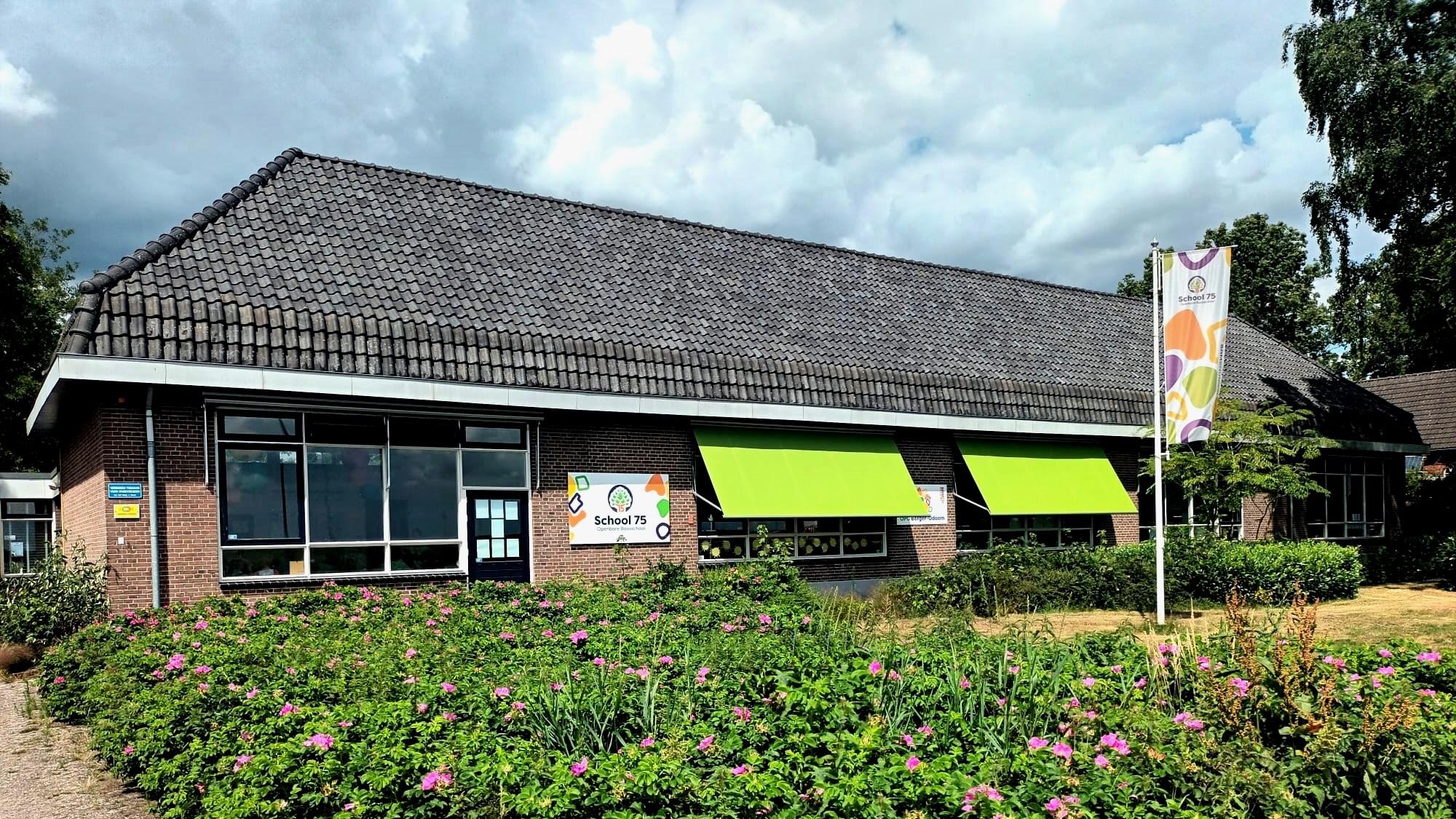 Openbare basisschool School 75 in Nieuw-Buinen, met groene zonneschermen en een bloeiende tuin. Openbare basisschool School 75 in Nieuw-Buinen, met groene zonneschermen en een bloeiende tuin.
