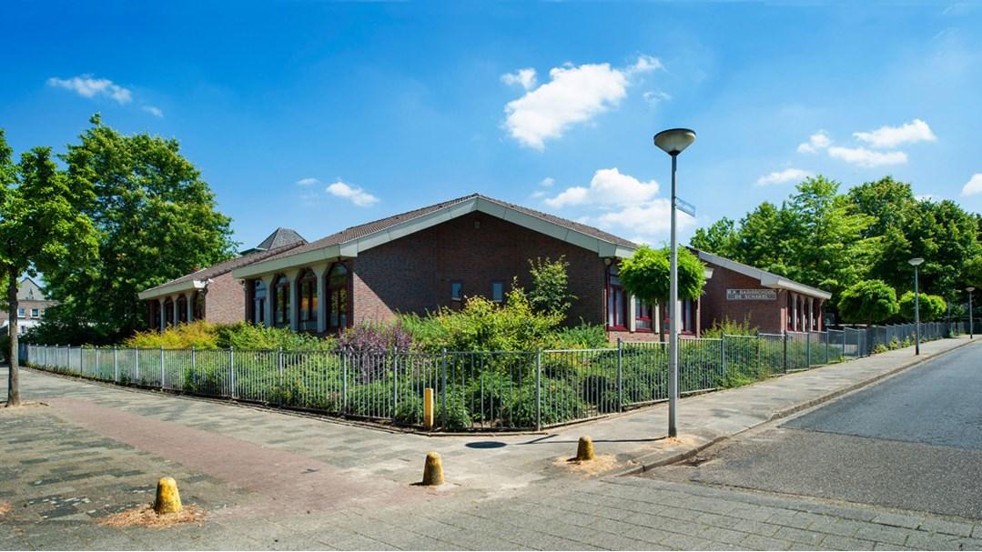 Rooms Katholieke Basisschool De Schakel in Heerlen, met een groen schoolplein en helder blauwe lucht. Rooms Katholieke Basisschool De Schakel in Heerlen, met een groen schoolplein en helder blauwe lucht.