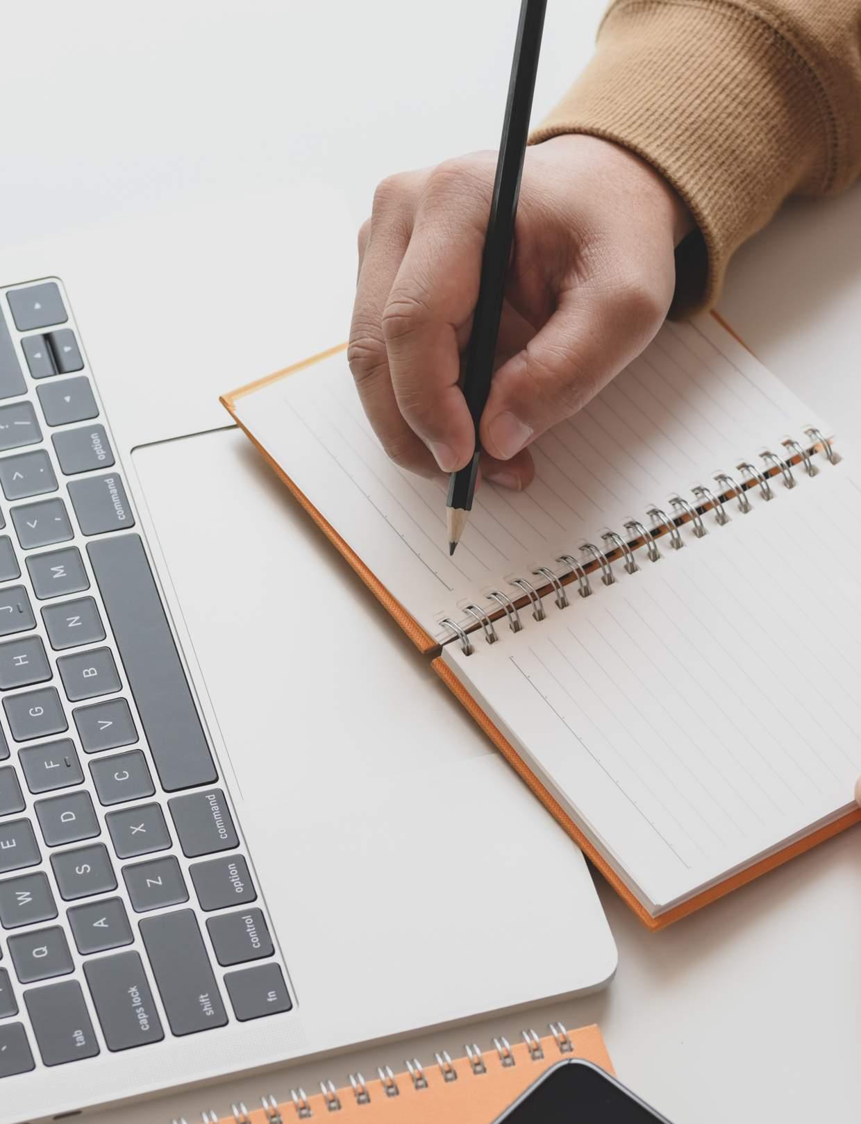 SBO Boulevard410 in Amersfoort: Een hand schrijft in een notitieboekje naast een laptop. SBO Boulevard410 in Amersfoort: Een hand schrijft in een notitieboekje naast een laptop.