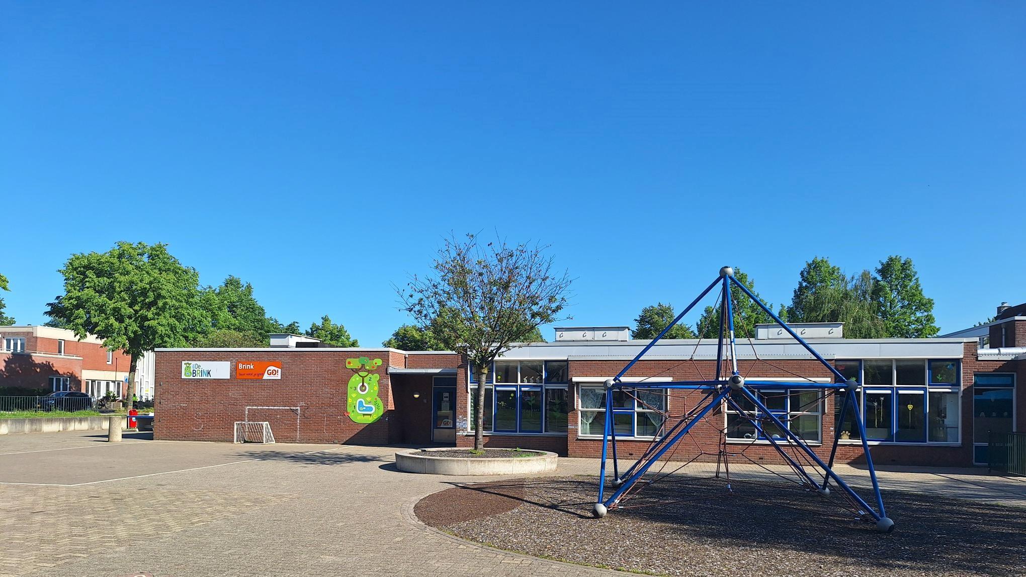 Schoolplein van De Brink in Lelystad met speeltoestellen en een heldere blauwe lucht.