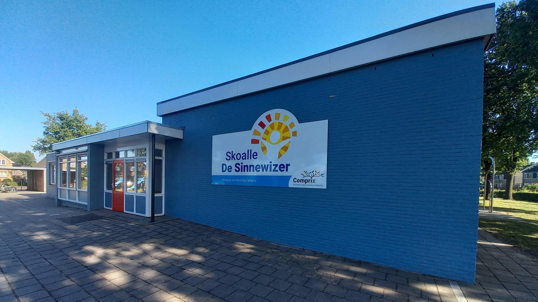 Skoalle de Sinnewizer in Wijnjewoude, met een helderblauwe gevel en duidelijk zichtbaar schoolbord. Skoalle de Sinnewizer in Wijnjewoude, met een helderblauwe gevel en duidelijk zichtbaar schoolbord.