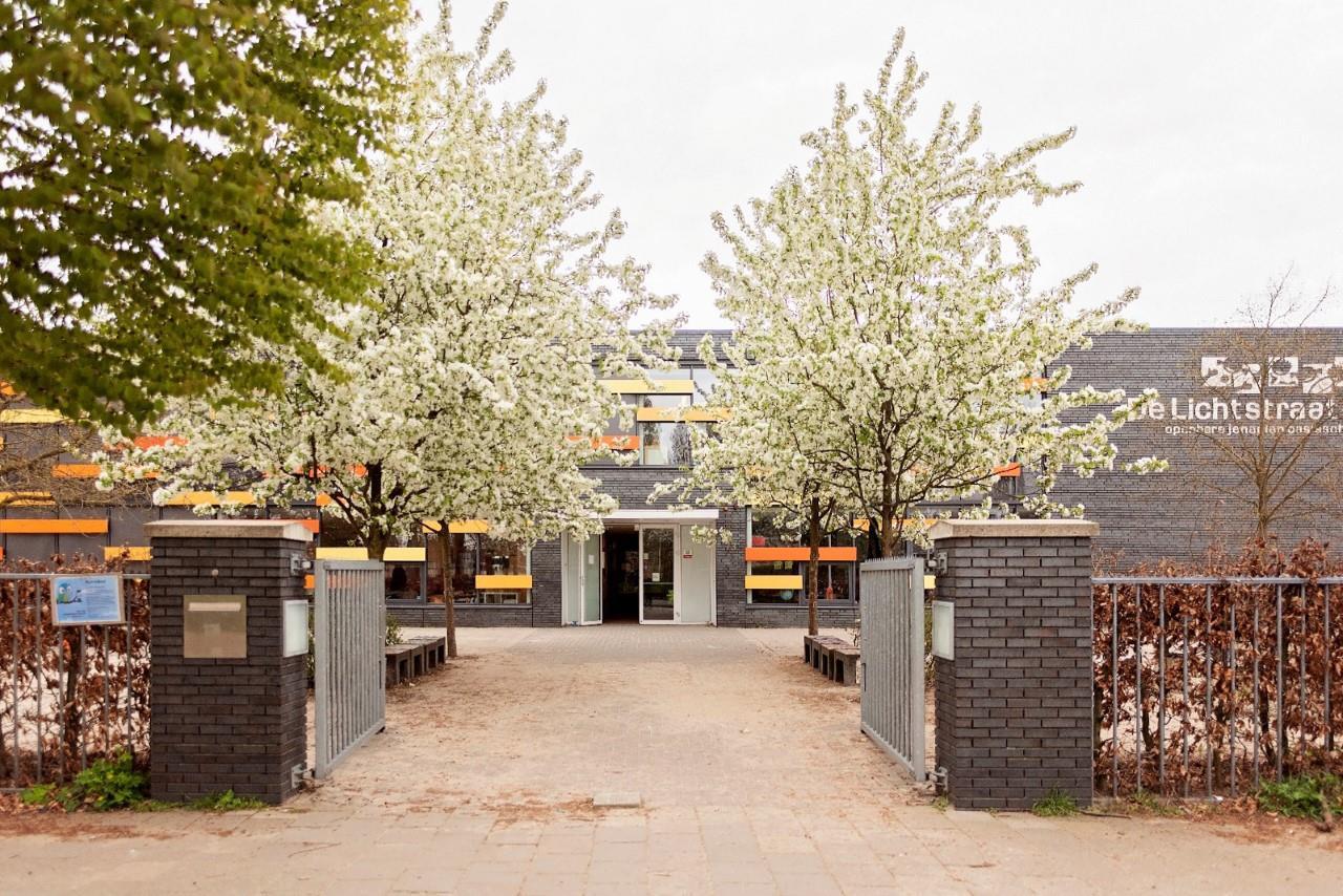 Toegangshek van Openbare Jenaplanschool De Lichtstraat in Vught, omringd door bloeiende bomen. Toegangshek van Openbare Jenaplanschool De Lichtstraat in Vught, omringd door bloeiende bomen.