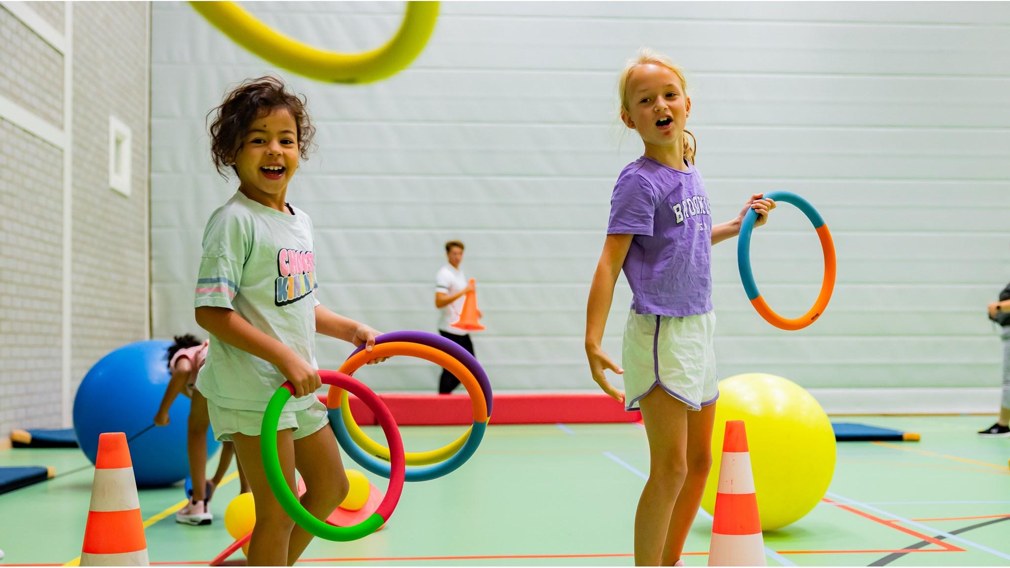 Twee blije kinderen spelen met hoepels in de gymzaal van de Da Costaschool in Hilversum. Twee blije kinderen spelen met hoepels in de gymzaal van de Da Costaschool in Hilversum.