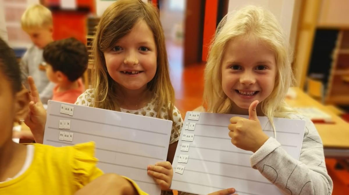 Twee blije kinderen van De Poseidon in Amsterdam tonen hun schrijfborden.