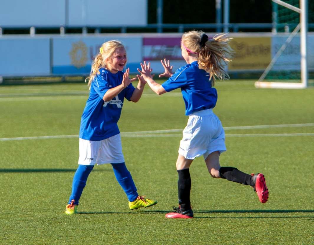 Twee blije meisjes in blauwe voetbalshirts vieren hun overwinning op het schoolplein van de Antoniusschool in Kudelstaart. Twee blije meisjes in blauwe voetbalshirts vieren hun overwinning op het schoolplein van de Antoniusschool in Kudelstaart.