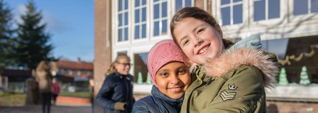 Twee blije meisjes omhelzen elkaar op het schoolplein van SBO 't Sterrenbos' in Dieren.
