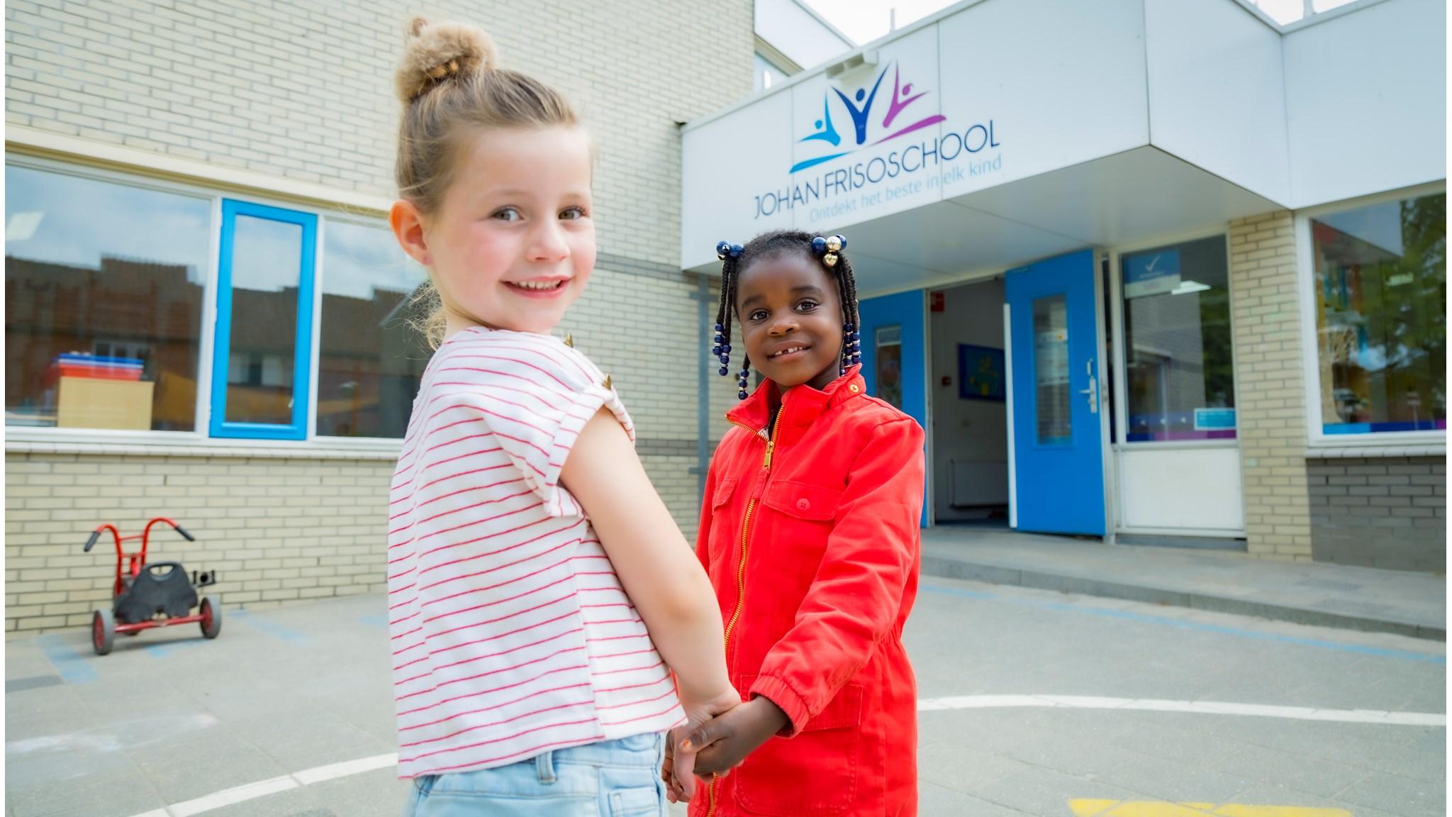Twee blije meisjes staan hand in hand op het schoolplein van de Johan Frisoschool in Woerden. Twee blije meisjes staan hand in hand op het schoolplein van de Johan Frisoschool in Woerden.