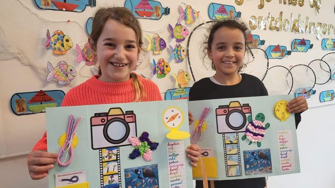 Twee blije meisjes tonen hun creatieve werk in de klas van Communityschool De Kameleon in Zwanenburg.