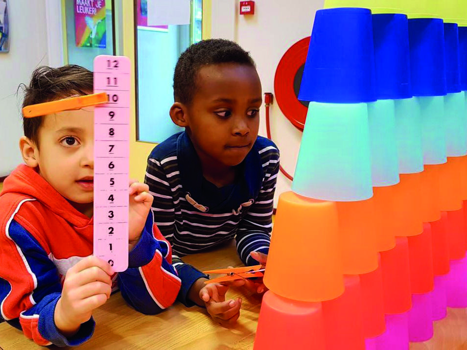 Twee kinderen aan het Kindcentrum het Rinket in Heemskerk spelen met kleurige bekers en een meetlat. Twee kinderen aan het Kindcentrum het Rinket in Heemskerk spelen met kleurige bekers en een meetlat.
