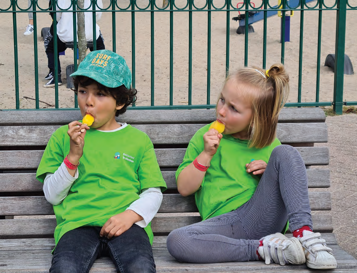 Twee kinderen in groene T-shirts genieten van een ijsje op de schoolplein van De Vlierboom in Den Haag. Twee kinderen in groene T-shirts genieten van een ijsje op de schoolplein van De Vlierboom in Den Haag.