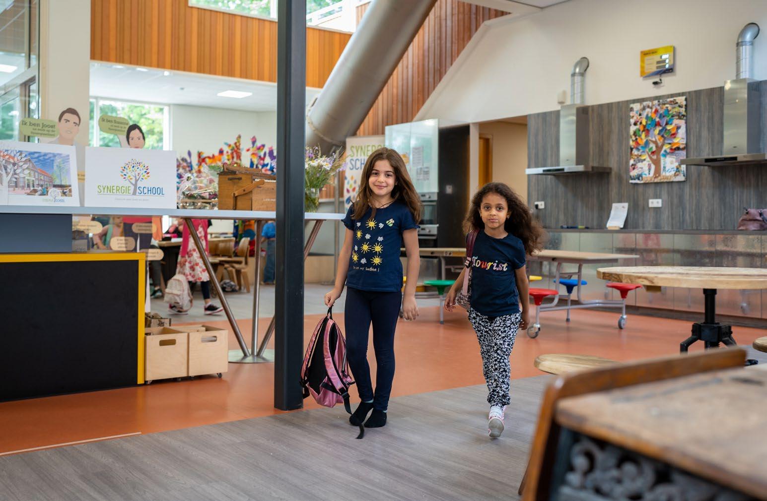 Twee kinderen lopen blij binnen in de Synergieschool St Alfonsus voor basisonderwijs in Roermond. Twee kinderen lopen blij binnen in de Synergieschool St Alfonsus voor basisonderwijs in Roermond.