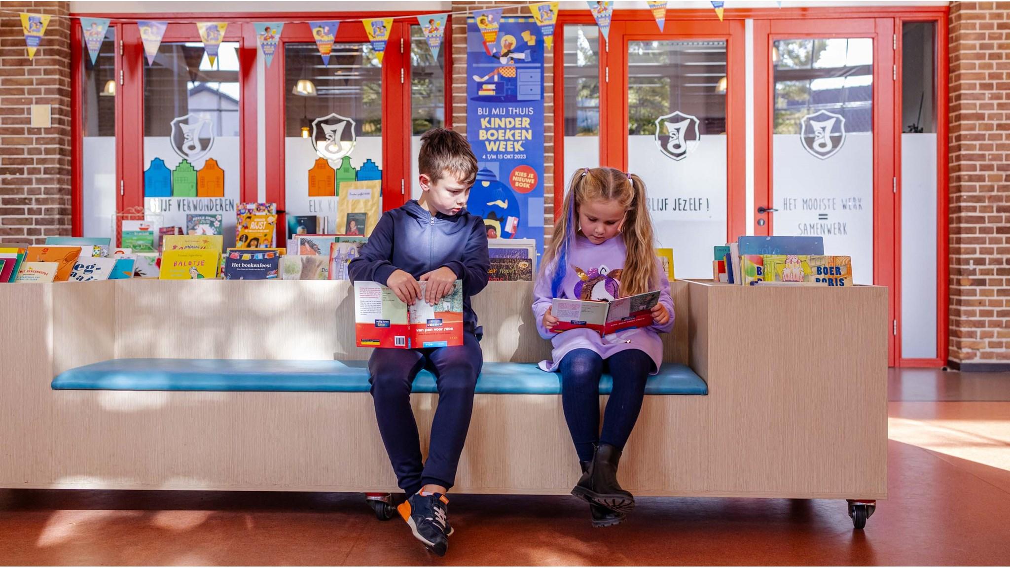 Twee kinderen zitten op een bank in IKC Sint Jan Hengelo terwijl ze boeken lezen. Twee kinderen zitten op een bank in IKC Sint Jan Hengelo terwijl ze boeken lezen.