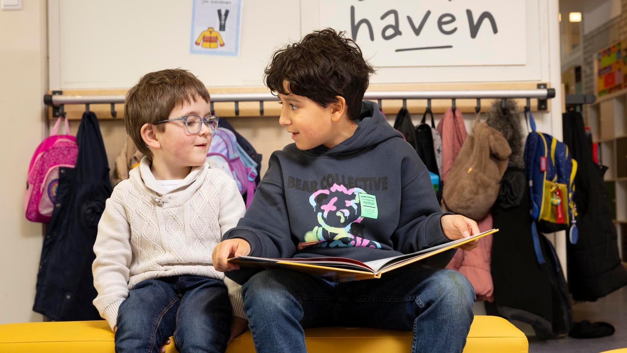 Twee kinderen zitten op een gele bank in de Delfshaven school in Rotterdam en bekijken samen een boek. Twee kinderen zitten op een gele bank in de Delfshaven school in Rotterdam en bekijken samen een boek.