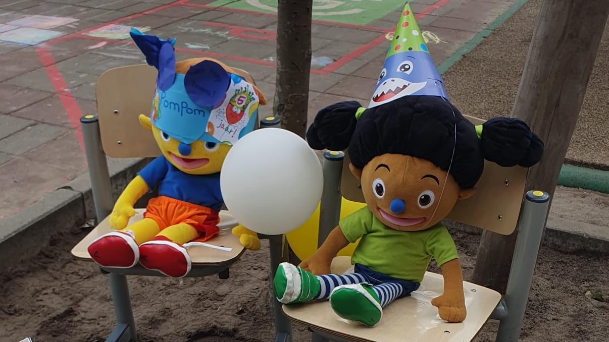 Twee knuffelpoppen met feesthoedjes zitten op stoelen in de speeltuin van De Rozemarn in Amsterdam. Twee knuffelpoppen met feesthoedjes zitten op stoelen in de speeltuin van De Rozemarn in Amsterdam.