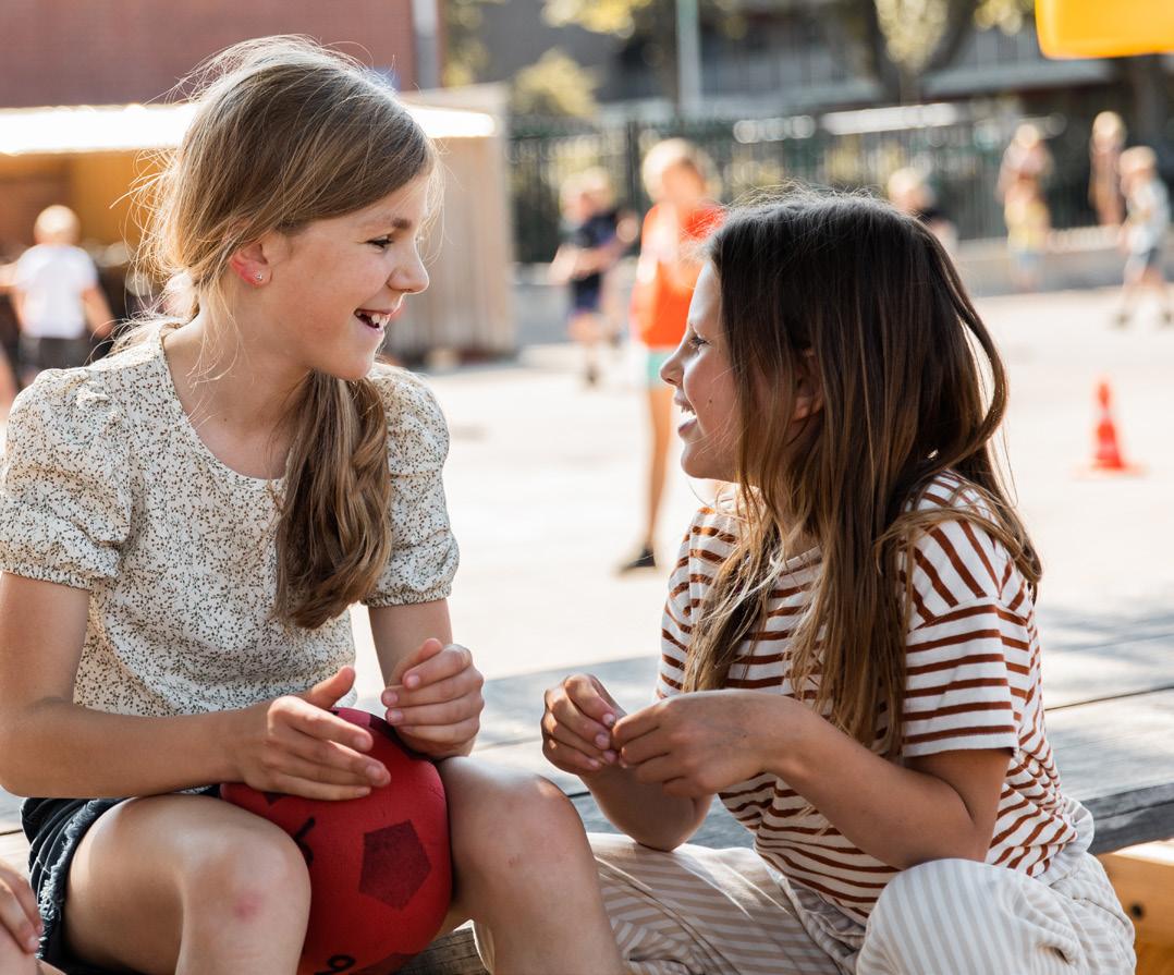 Twee lachende meisjes spelen op het schoolplein van de Paasbergschool in Ede.
